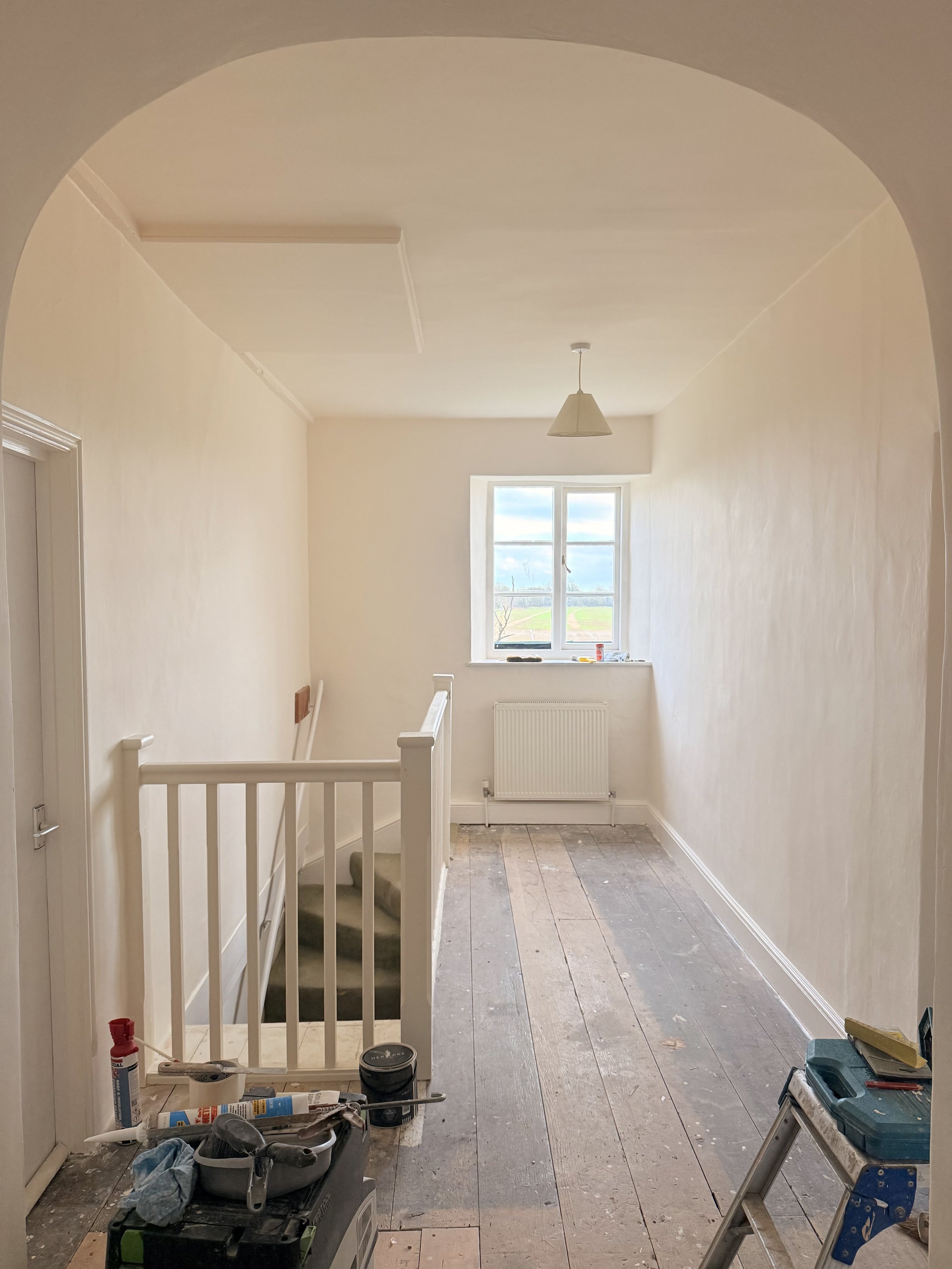 Empty room under renovation with a small staircase, window showing outdoor landscape, and tools on the floor.