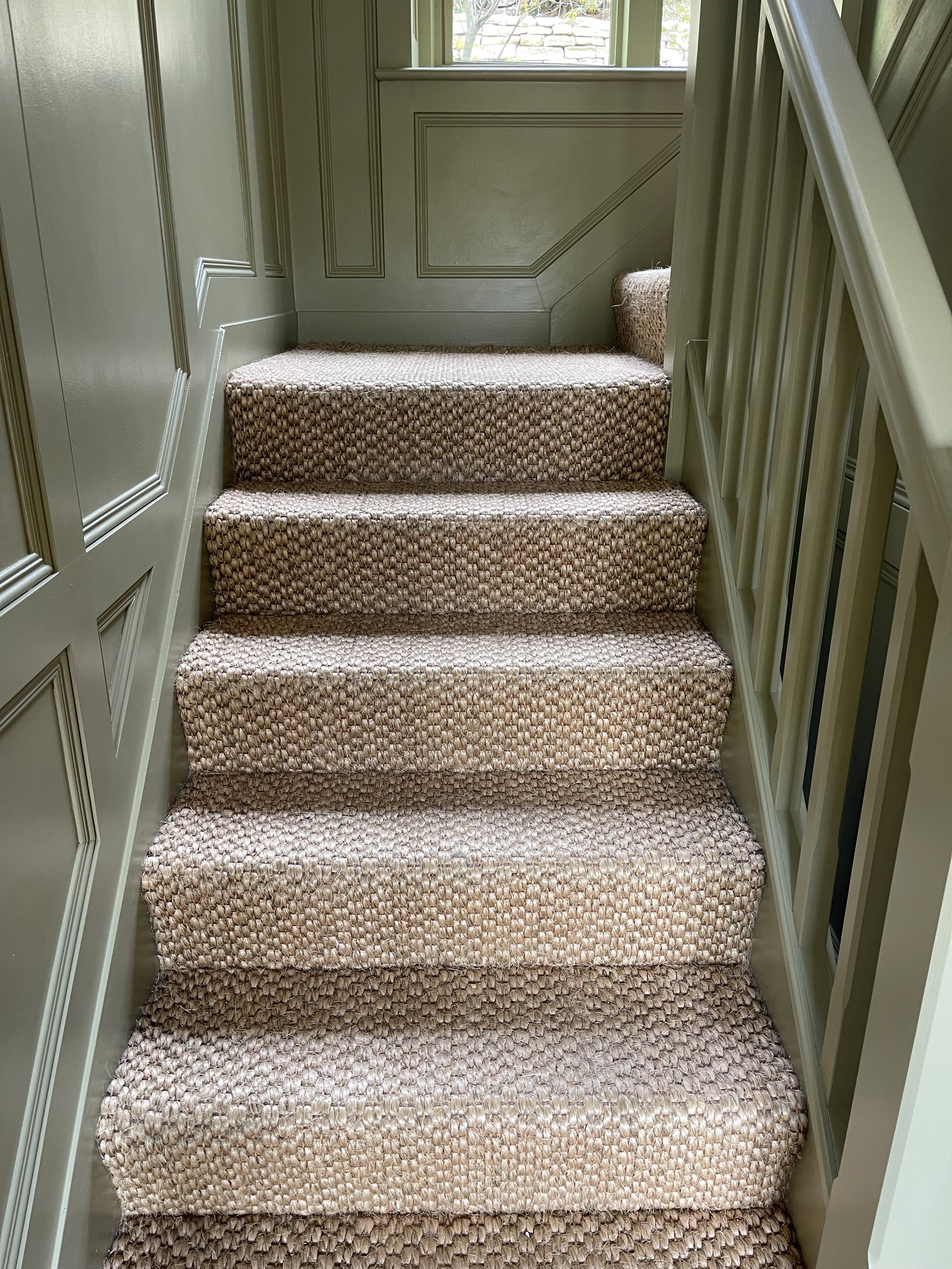 Carpeted staircase leading up to a window with a view of a stone wall.