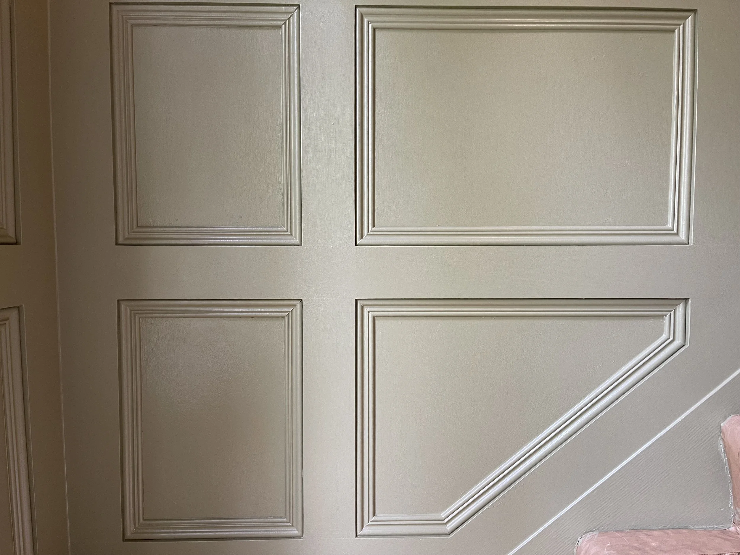 A beige wall with decorative molding panels and a section of pink upholstery fabric visible at the bottom right corner.