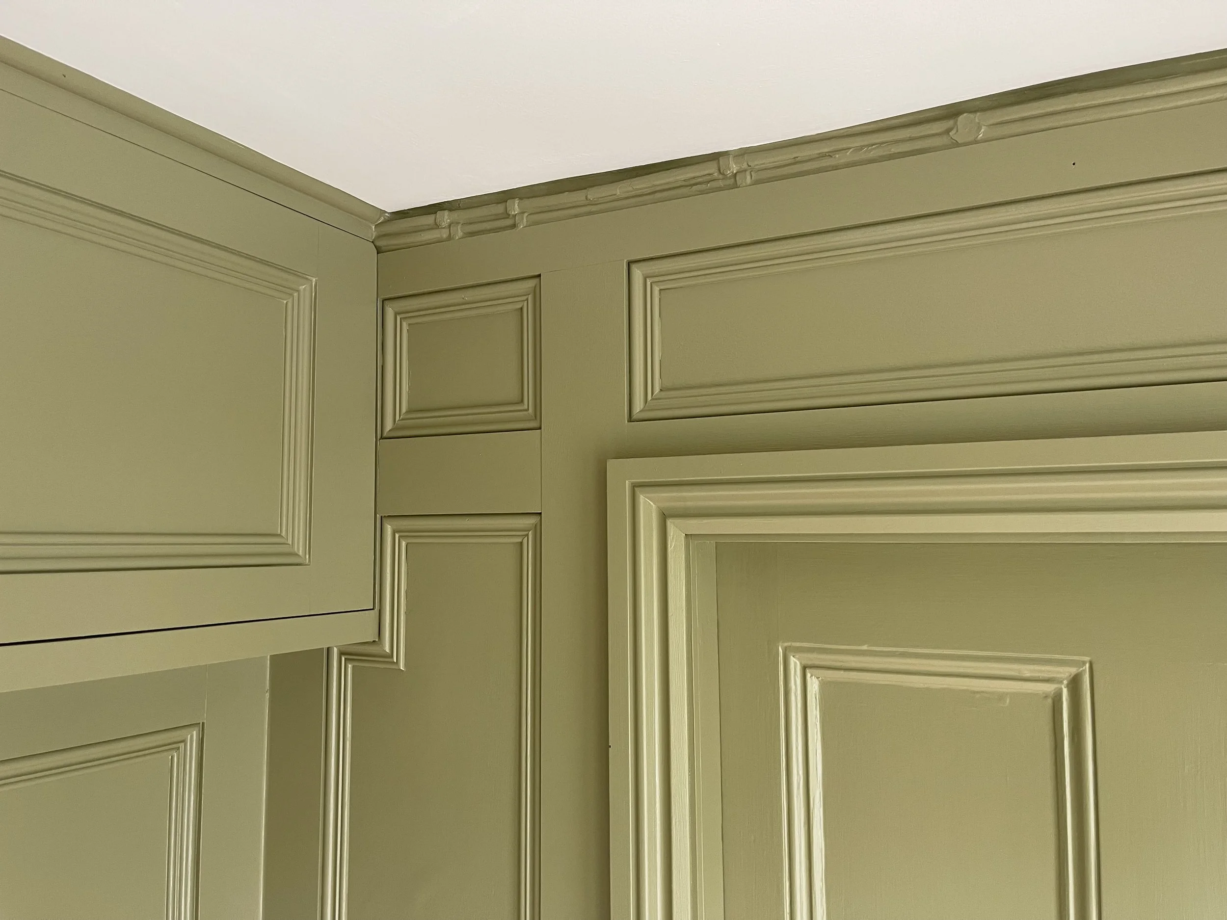 Close-up of a corner with green painted wooden cabinets and crown molding along the ceiling.