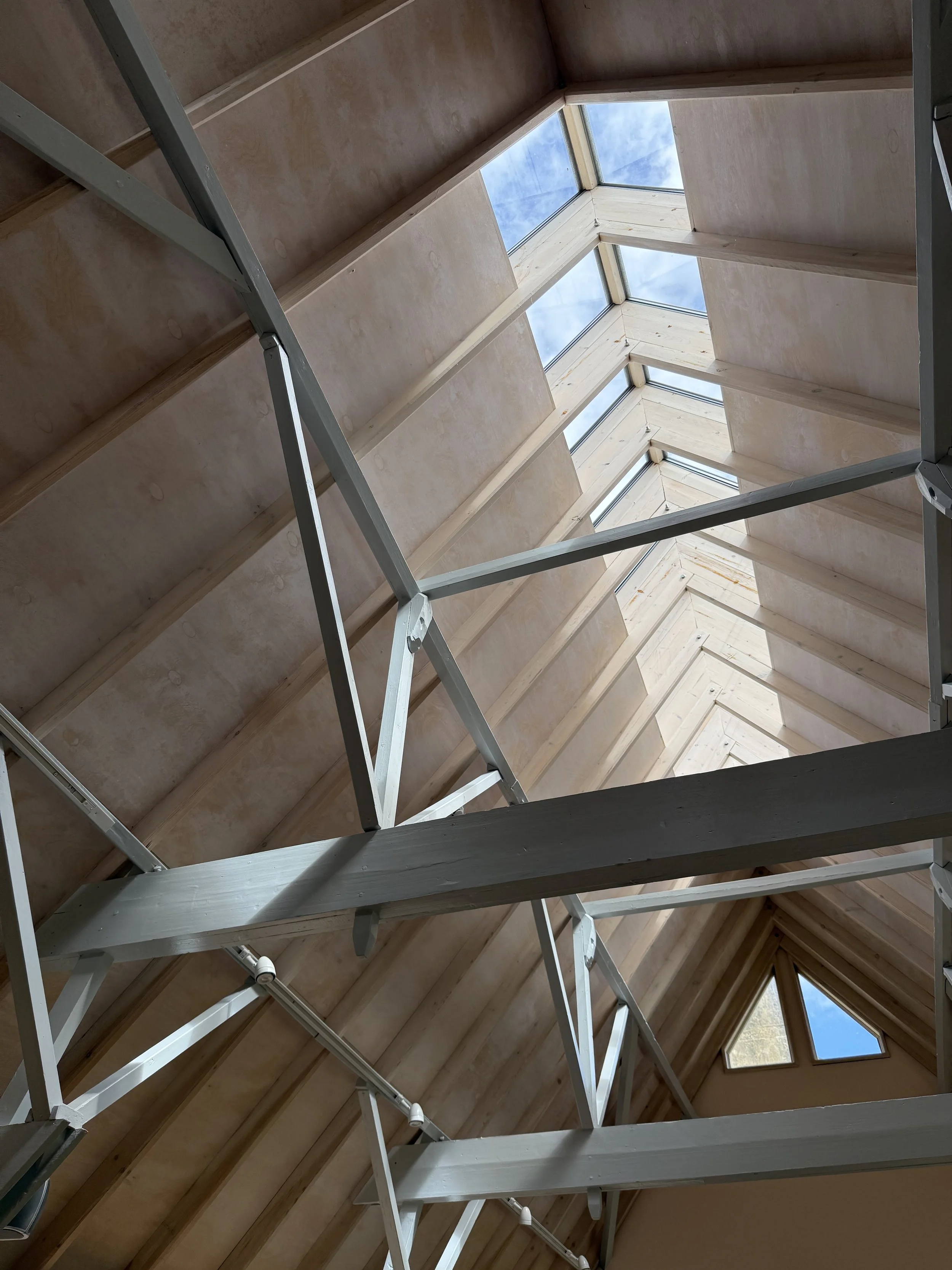 Looking up at a wooden attic roof with skylights and metal support beams.
