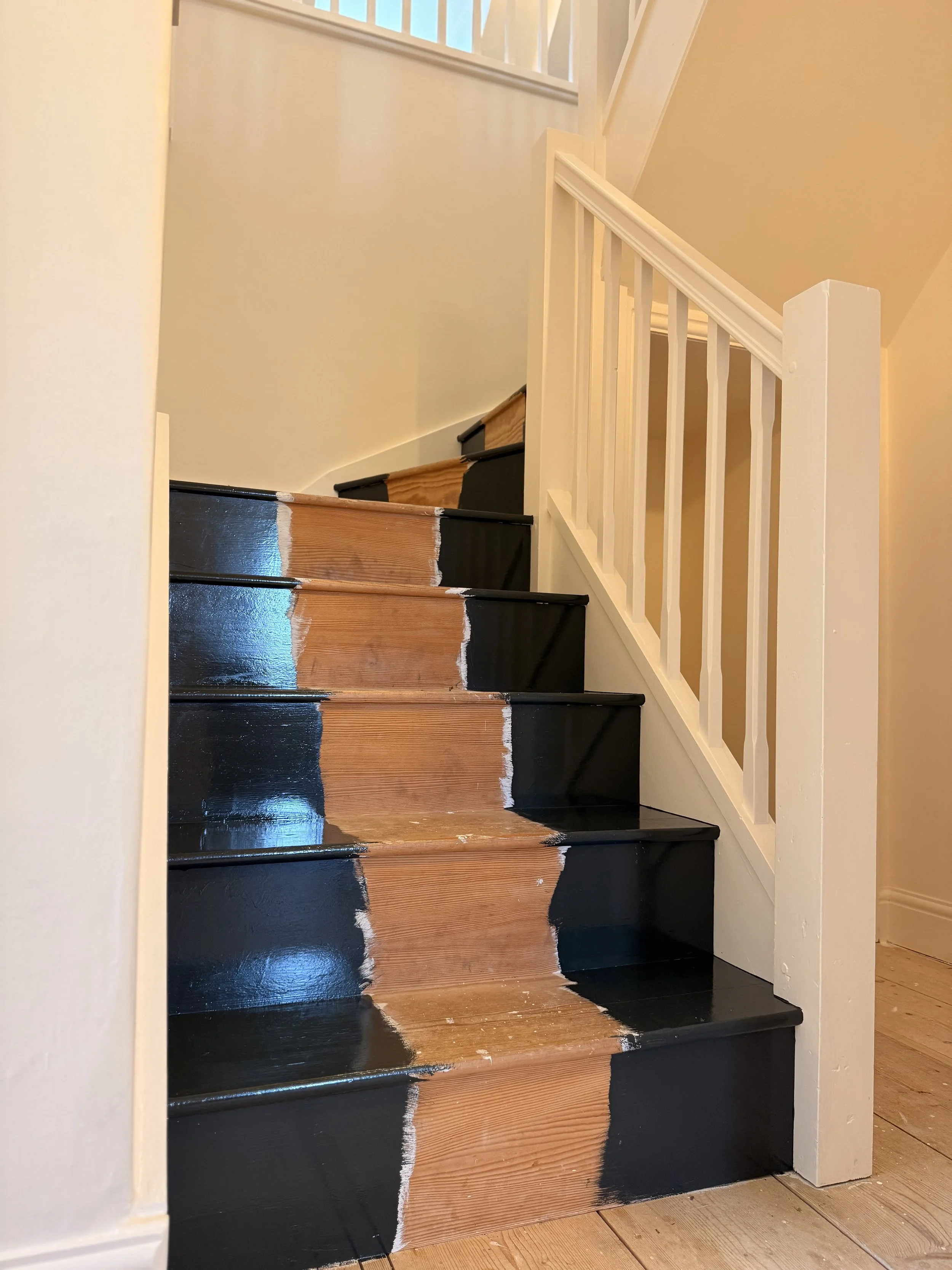 Staircase in the process of being painted, with black paint on the bottom part and unpainted wooden steps in the middle.