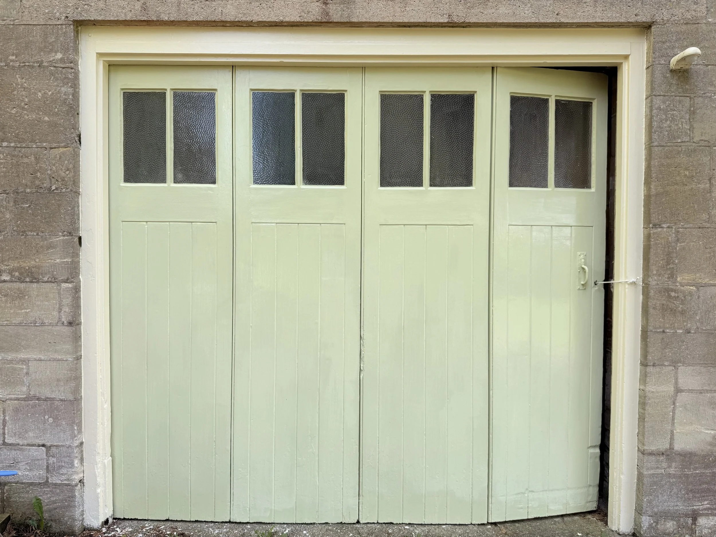 A pale green garage door with small textured glass windows at the top, surrounded by a concrete wall.
