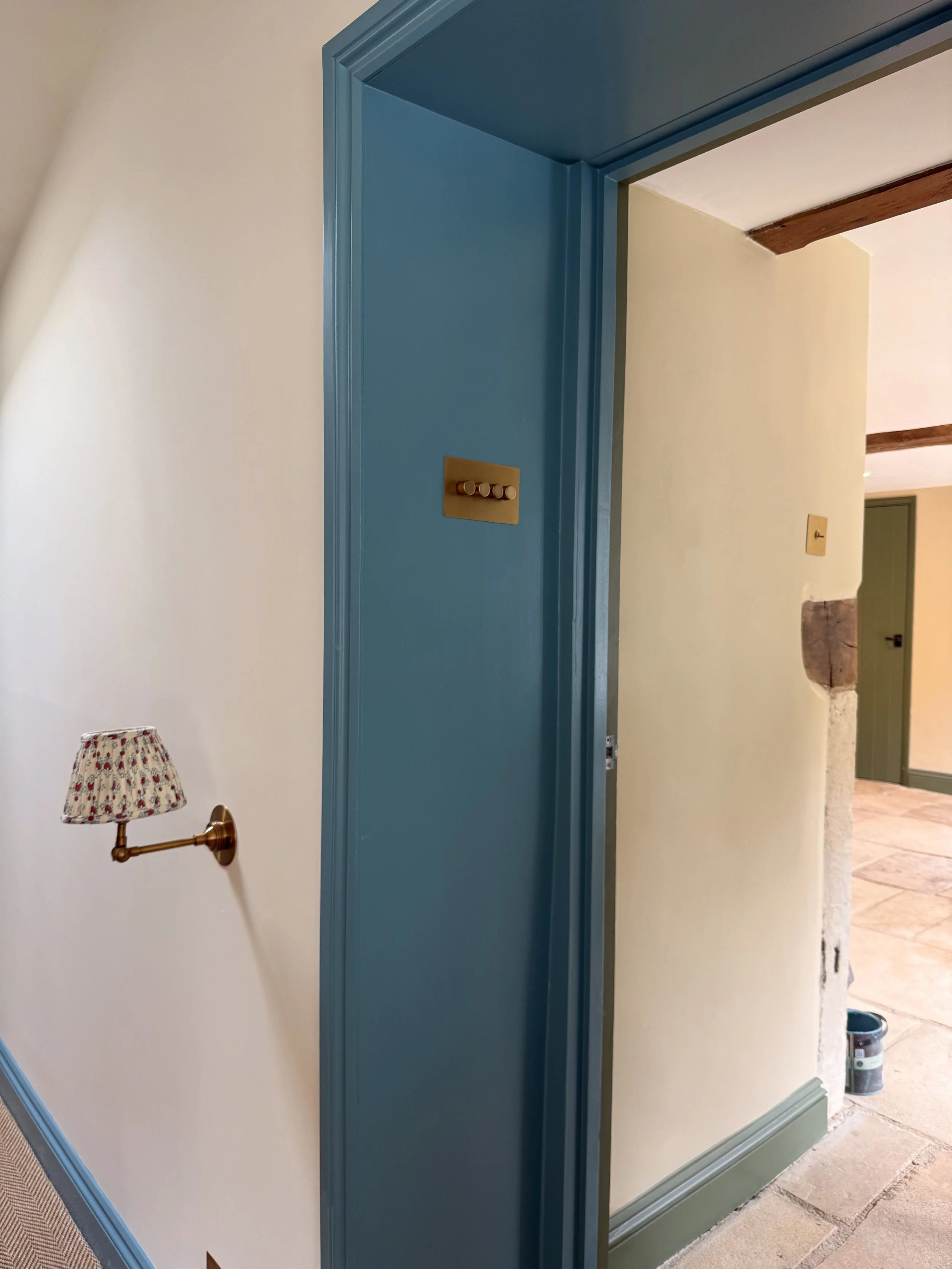Interior view of a doorway with blue trim, beige walls, and a small wall-mounted lamp with a floral lampshade.