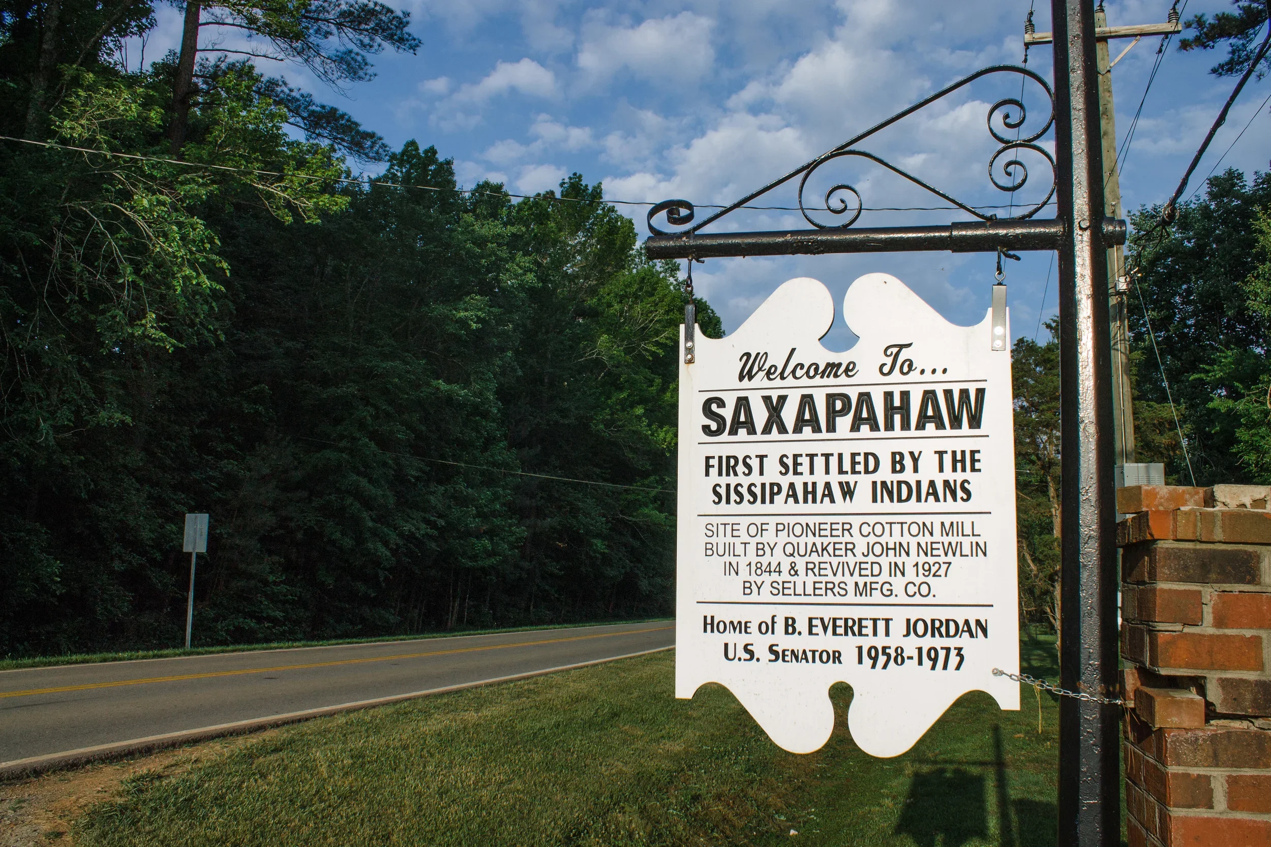 Welcome sign for Saxapahaw, North Carolina, mentioning its history as the first settled area by the Sissipahaw Indians, site of a cotton mill built by Quaker John Newlin, and home of B. Everett Jordan, U.S. Senator.