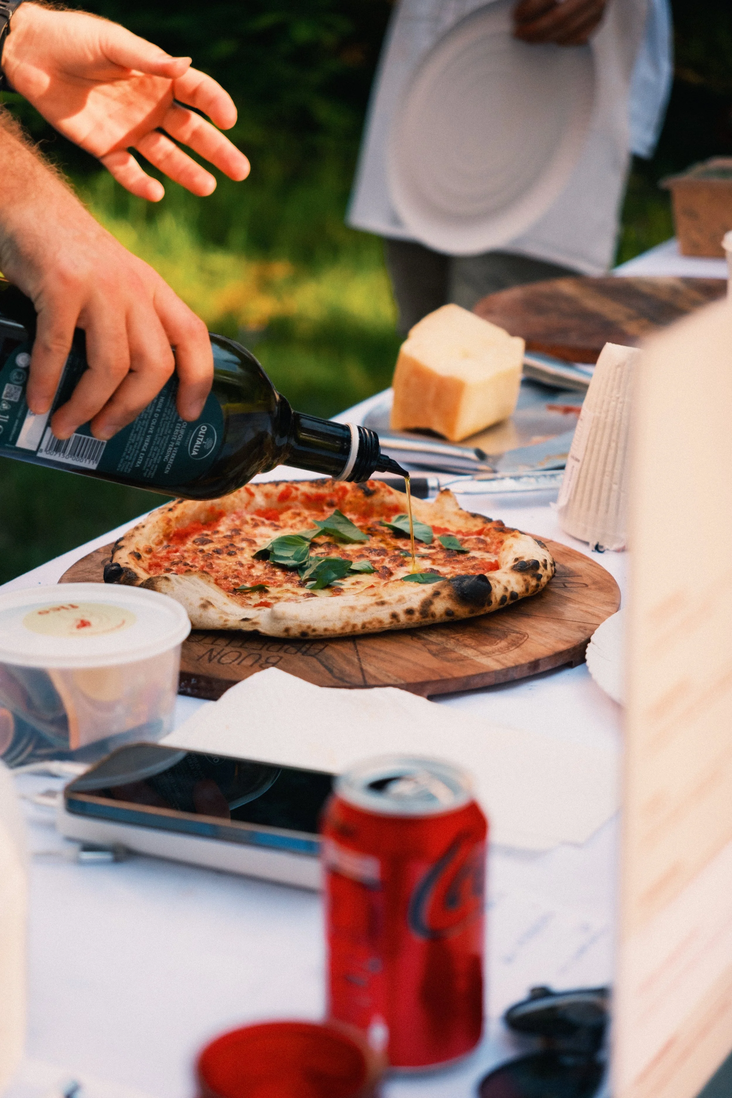 Person pouring olive oil on a freshly baked pizza with basil leaves.