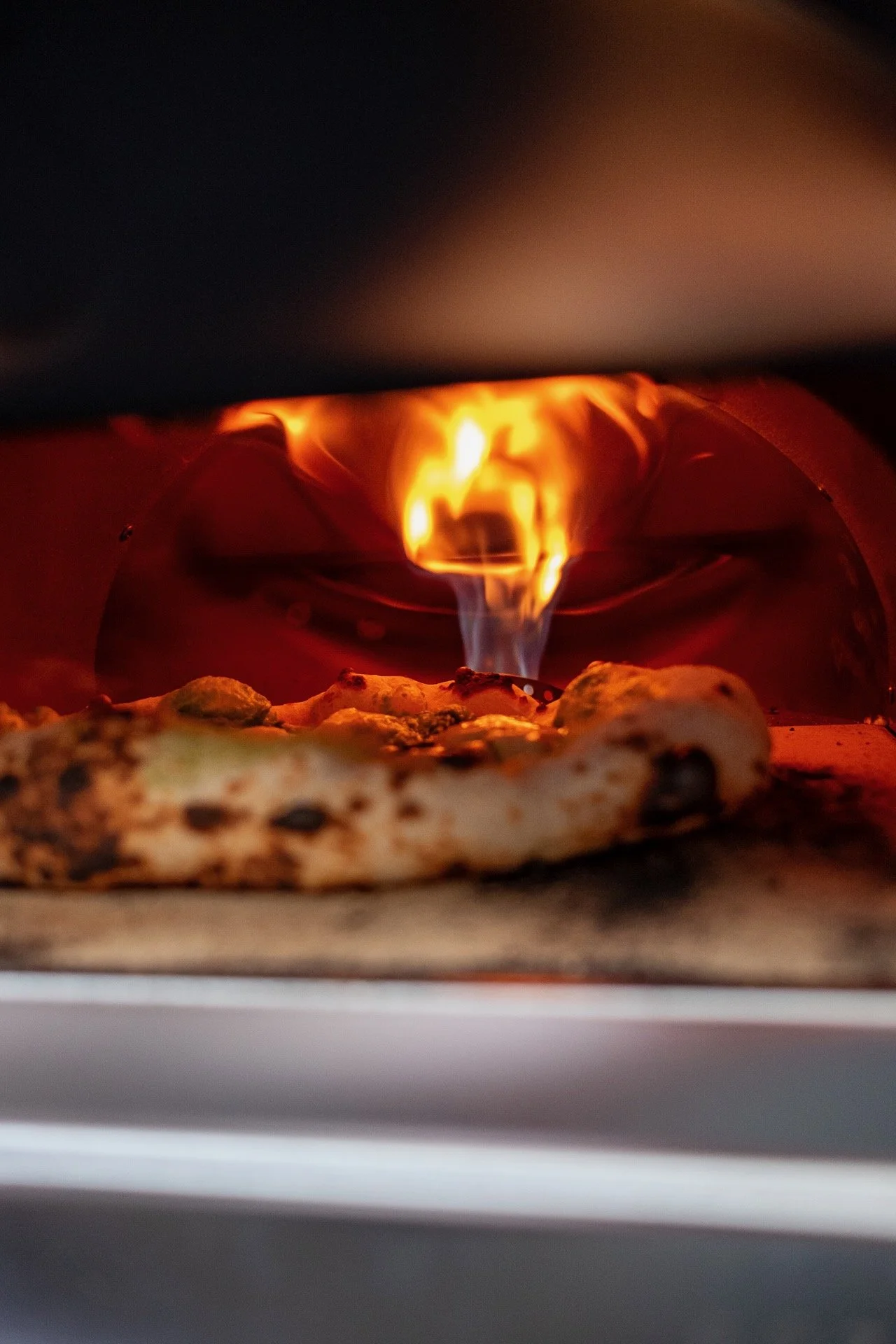 Een verse pizza in Napolitaanse stijl in een steenoven met een zichtbare vlam.
