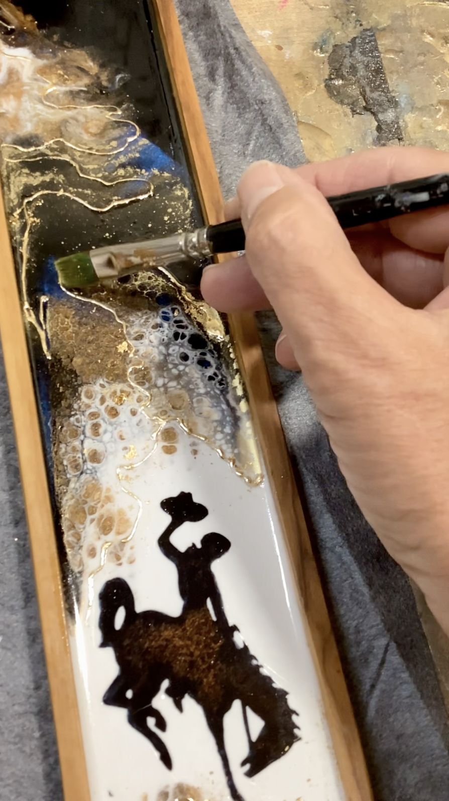 Artist applying 24K gold accents to a handmade Wyoming charcuterie board with resin artwork.