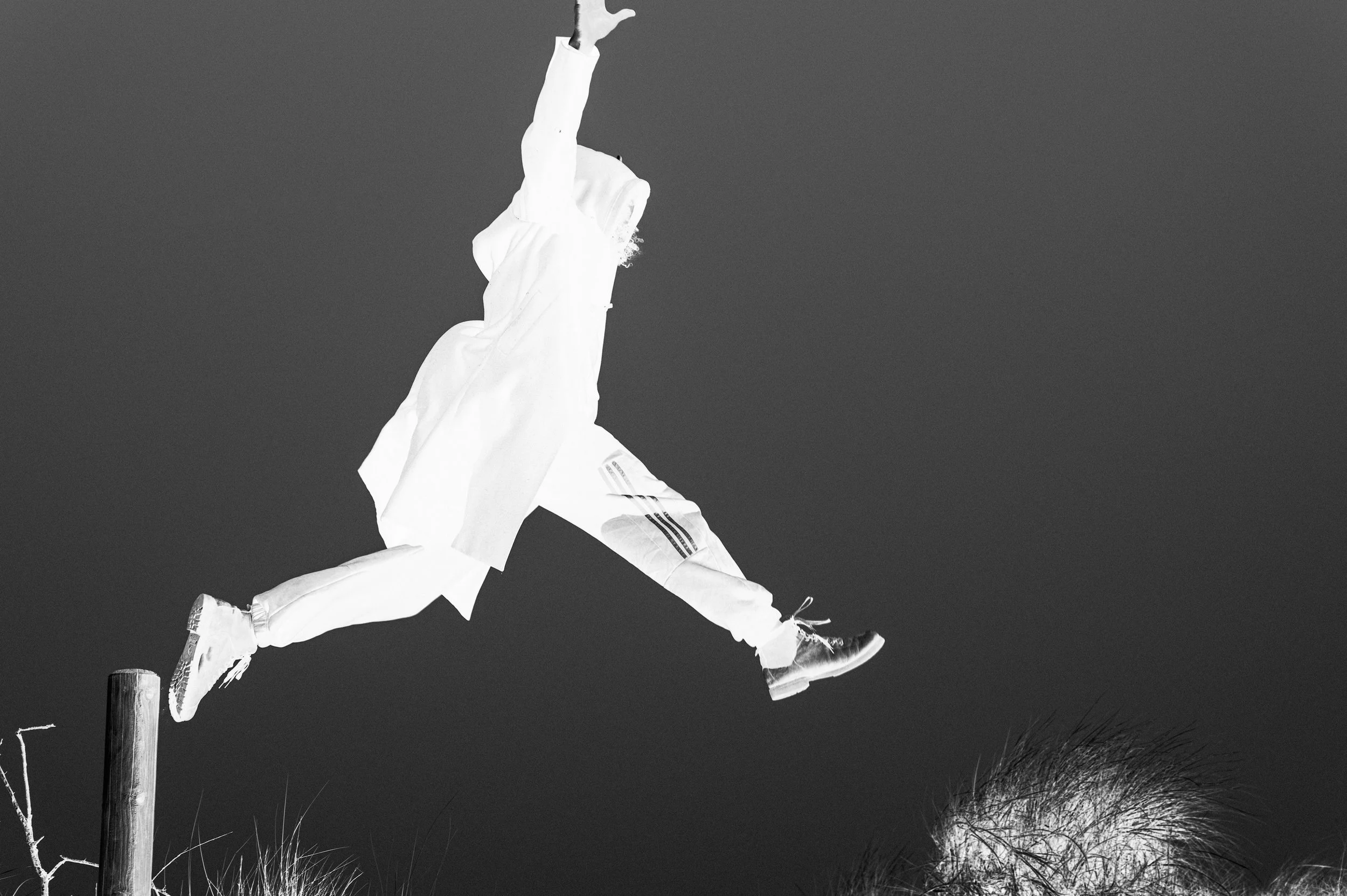 Person jumping off a wooden post on a hill, captured in black and white with a dark sky background.