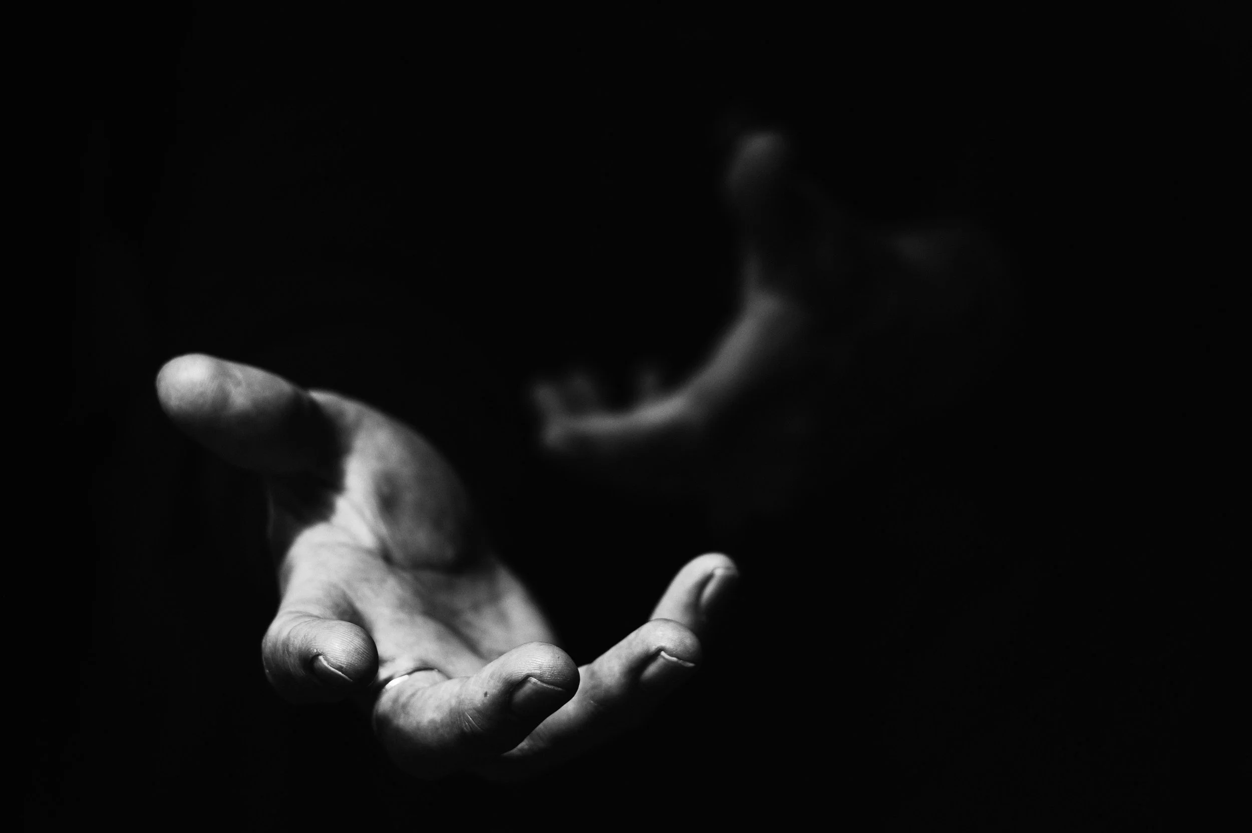 A black and white image of a hand reaching out with fingers extended, in a dark environment with the finger pressed against a surface or object.