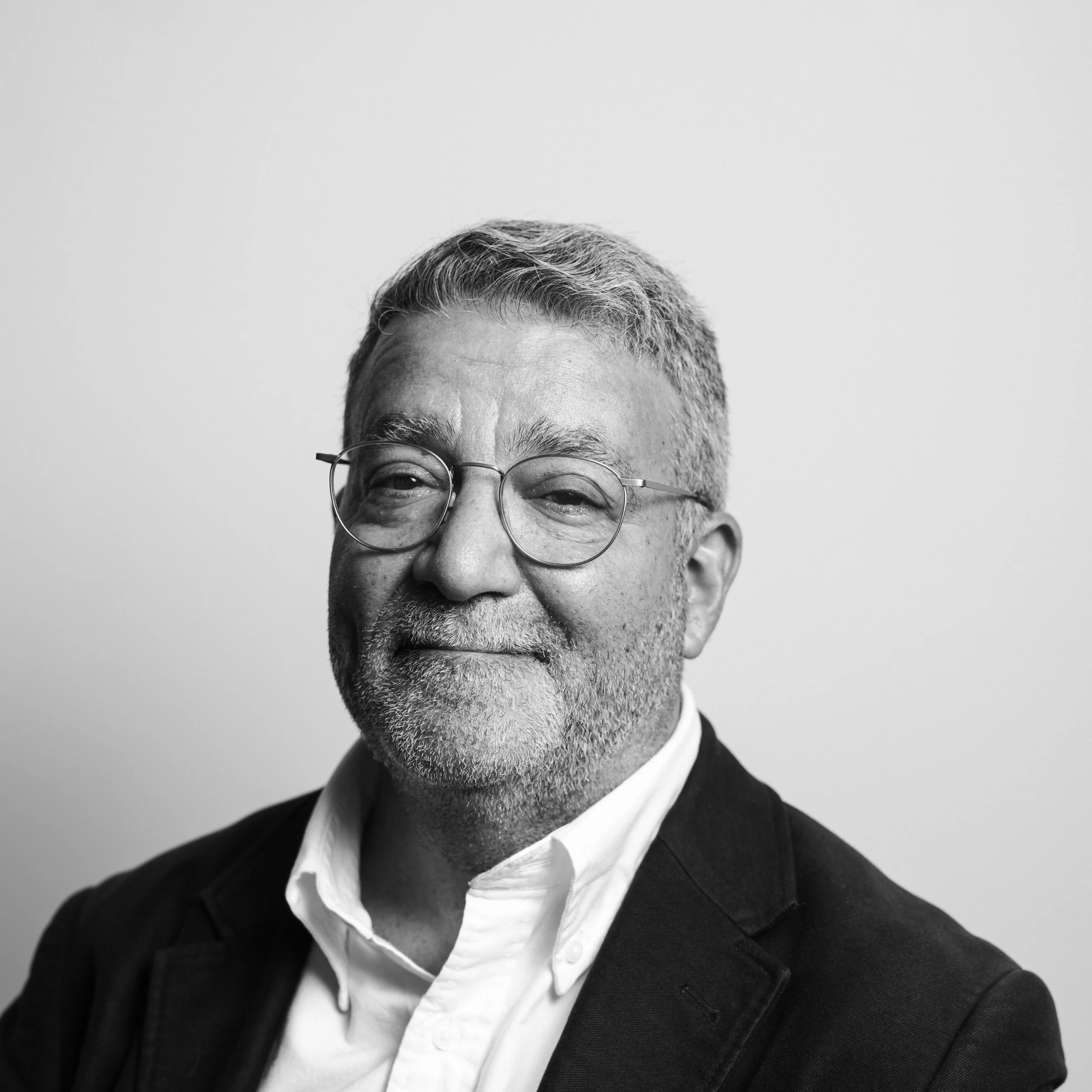 Close-up black-and-white portrait of a smiling man with short gray hair, glasses, dressed in a suit and white shirt.