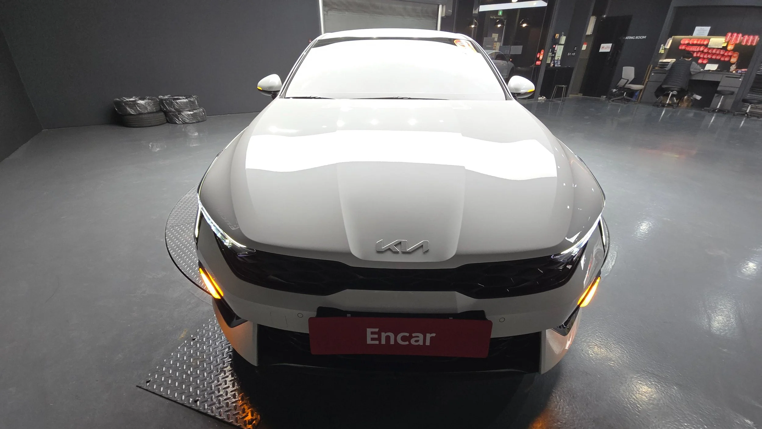 Front view of a silver Kia car in a showroom with a red Encar sign.