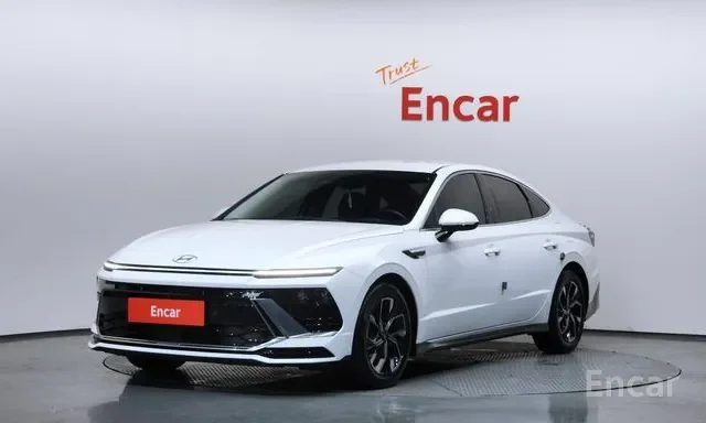 White Hyundai electric sedan with black accents in a showroom, with 'Trust Encar' signage on the wall behind it.