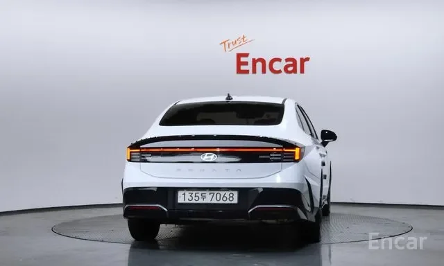 White Hyundai Ioniq 5 electric vehicle on a rotating display platform in a showroom with the words 'Trust Encar' written behind and above the car.