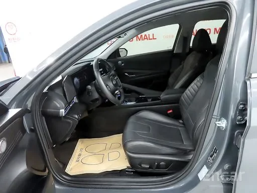 Interior of a modern gray car showing the driver's seat, steering wheel, and front passenger seat with a paper floor mat on the driver's side.