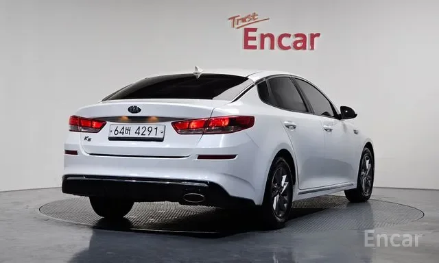 White modern sedan car in a showroom with Encar branding on the wall behind it.