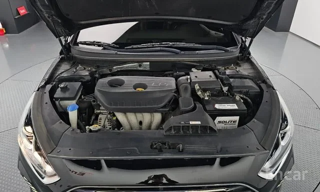 Open car hood showing engine bay with engine cover, battery, and various engine components.