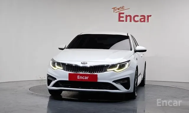 White Kia sedan in a showroom with a red Encar sign on the wall behind it.