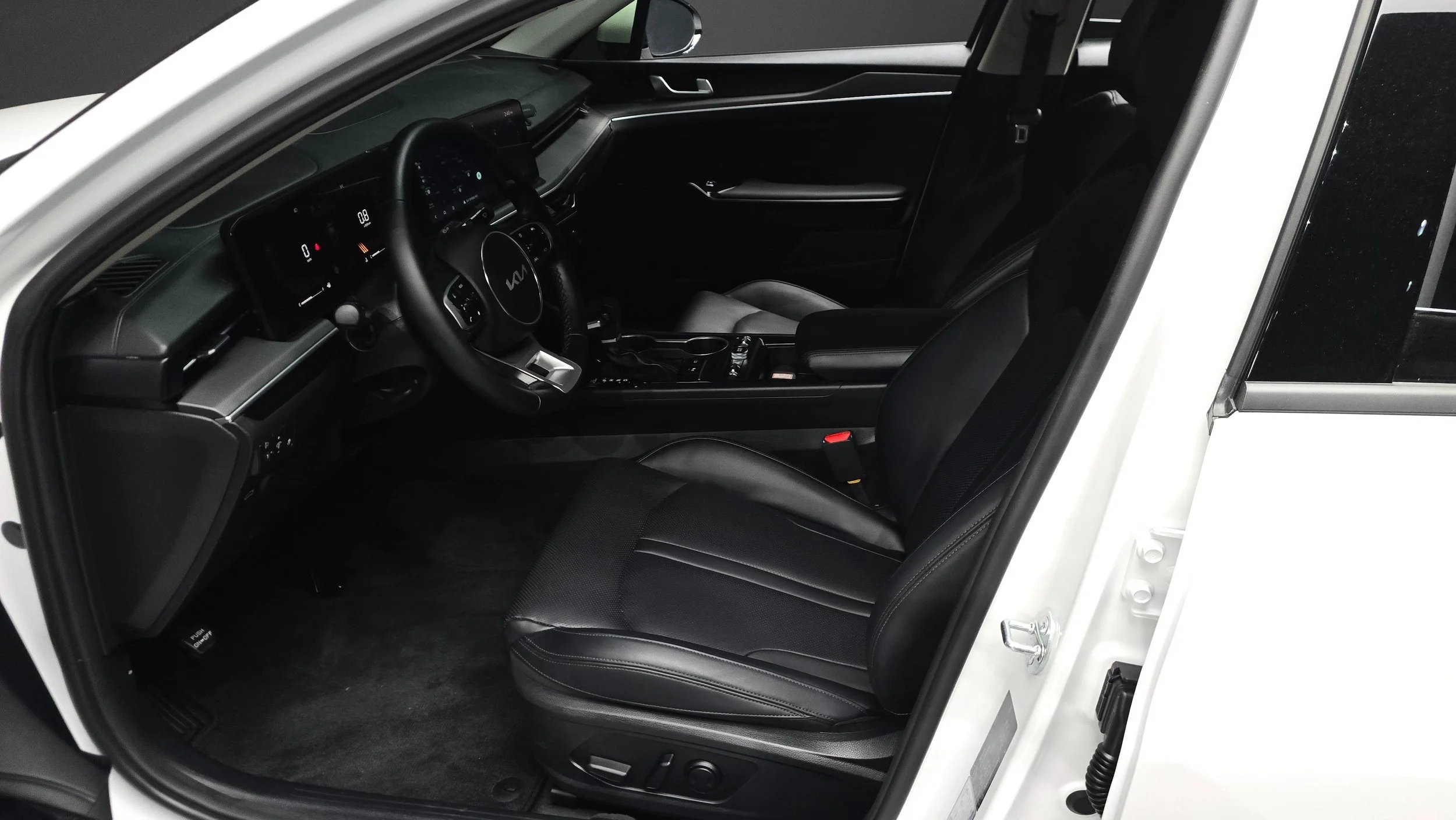Interior of a modern vehicle showing the black leather driver's seat, steering wheel, dashboard, and center console with gear shifter and controls.