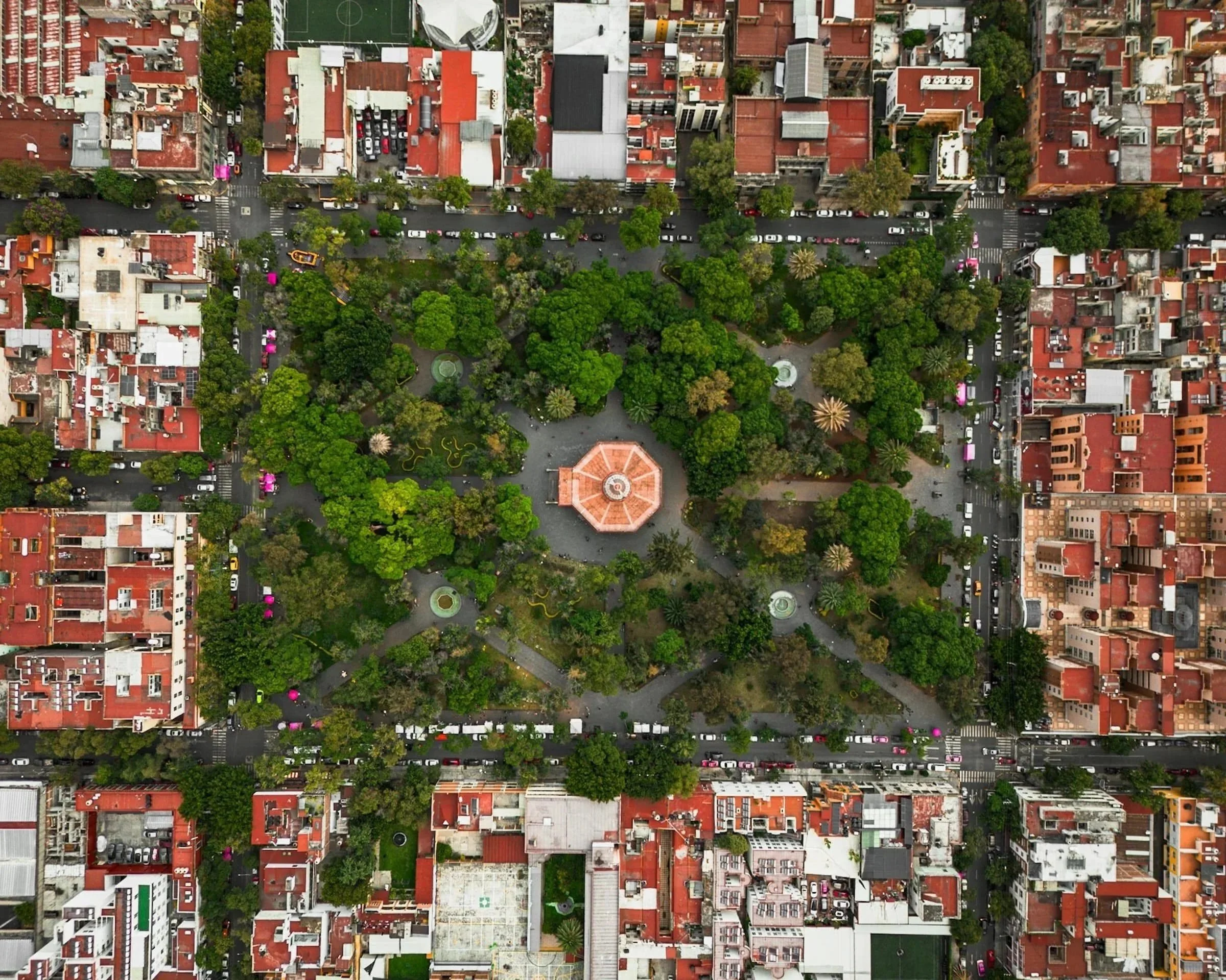 Aerial view of a city park in Mexico City with a gazebo surrounded by trees, pathways, and urban buildings with red roofs.