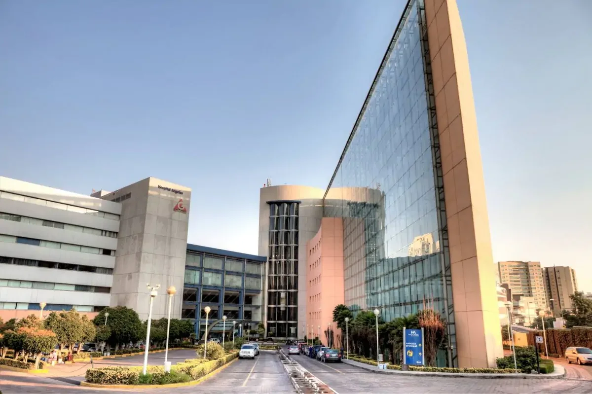 Modern hospital building with a glass facade and surrounding parking lot.
