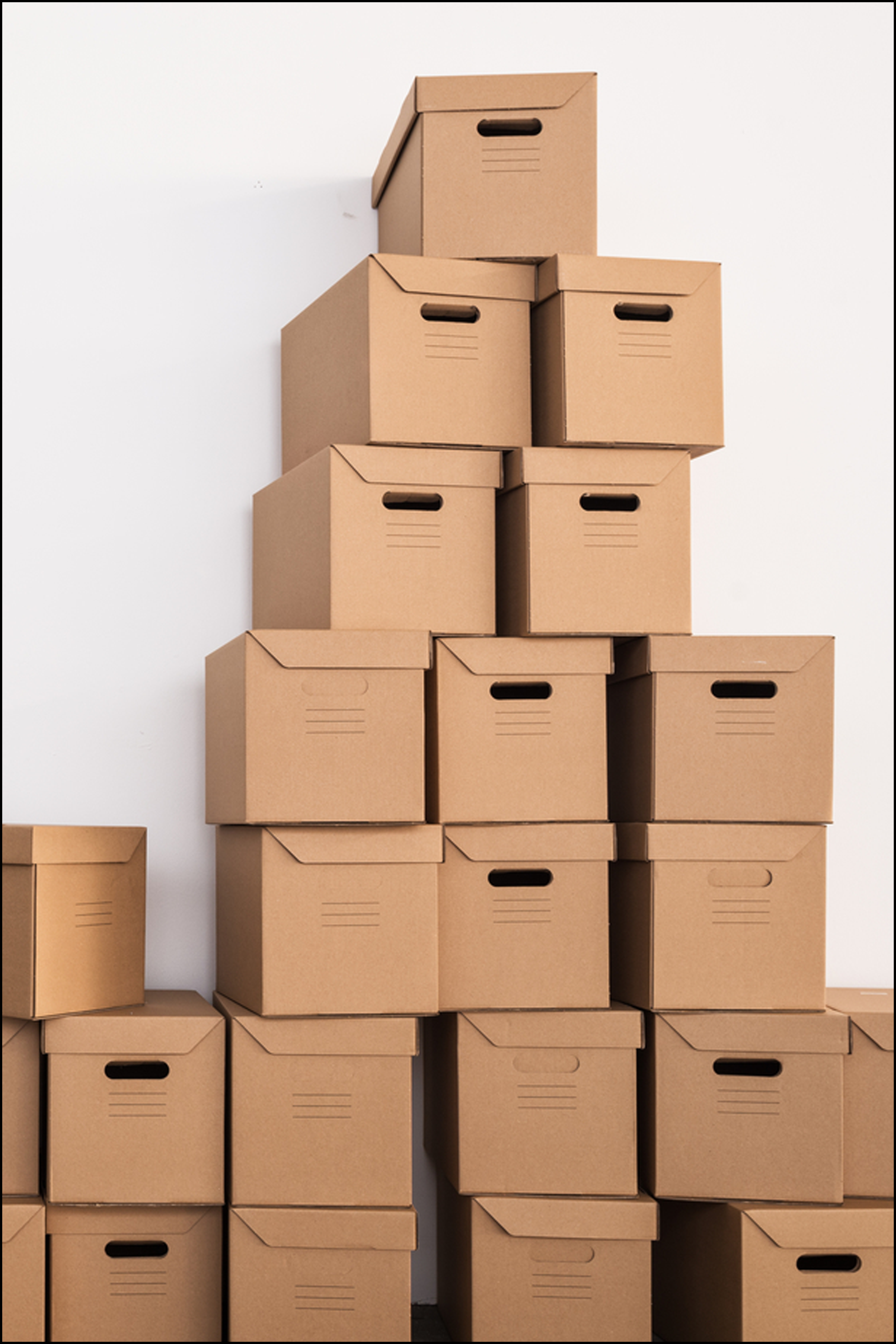 Stacked cardboard storage boxes arranged in a pyramid shape against a white wall.