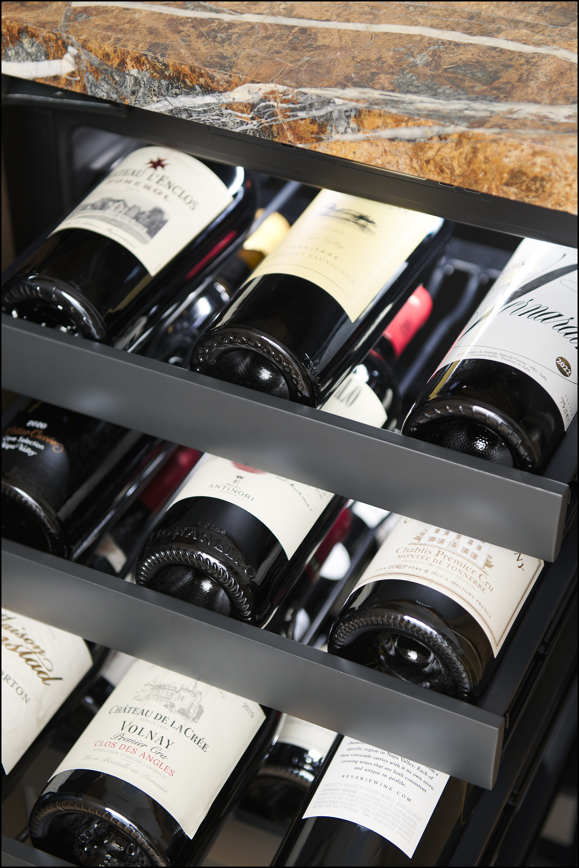 Multiple wine bottles arranged on a wine rack with a marble countertop above.