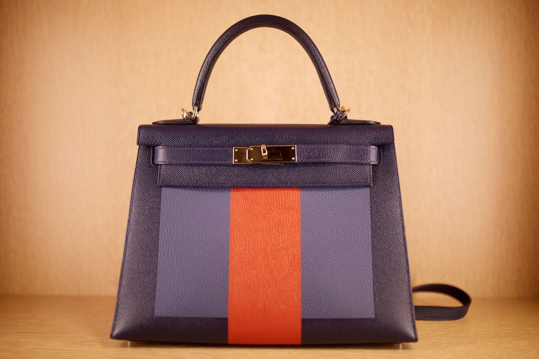 A designer handbag with a purple base and a vertical orange stripe, set against a wooden background.