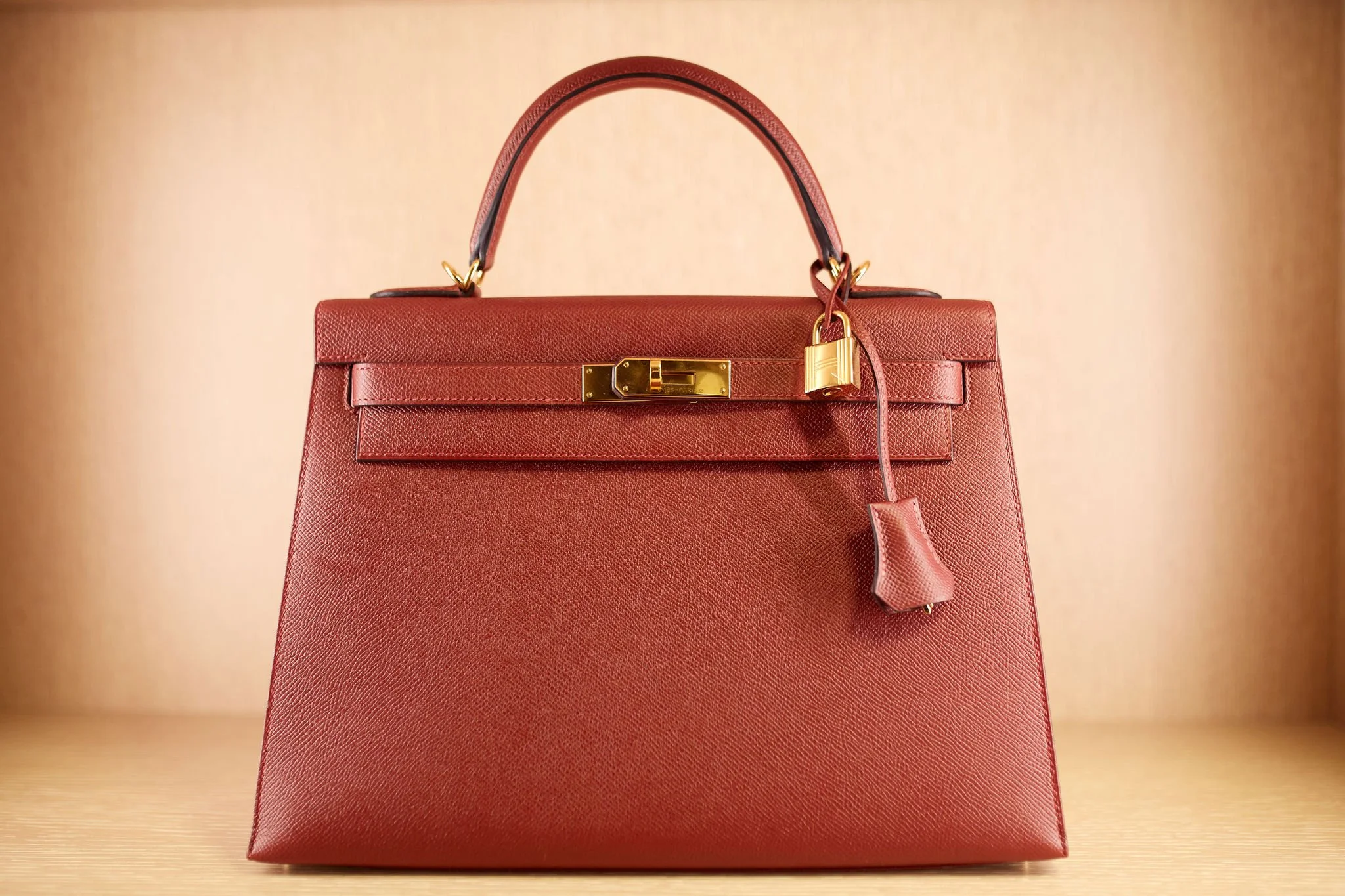 Red designer handbag with gold hardware and a textured surface, placed on a wooden surface with a plain beige background.