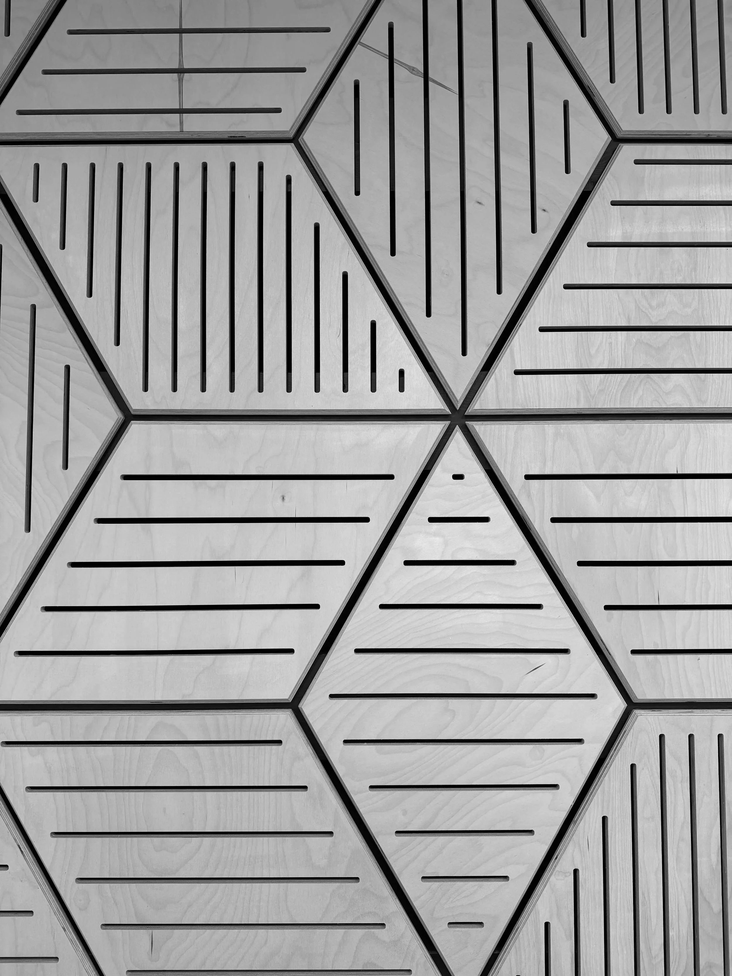 Pattern of hexagonal tiles with horizontal black lines on a light wood surface.