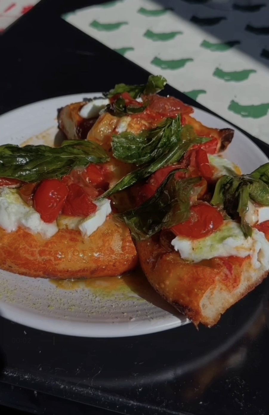 Close-up of two slices of Margherita pizza with tomatoes, basil, cheese, and sauce on a white plate.
