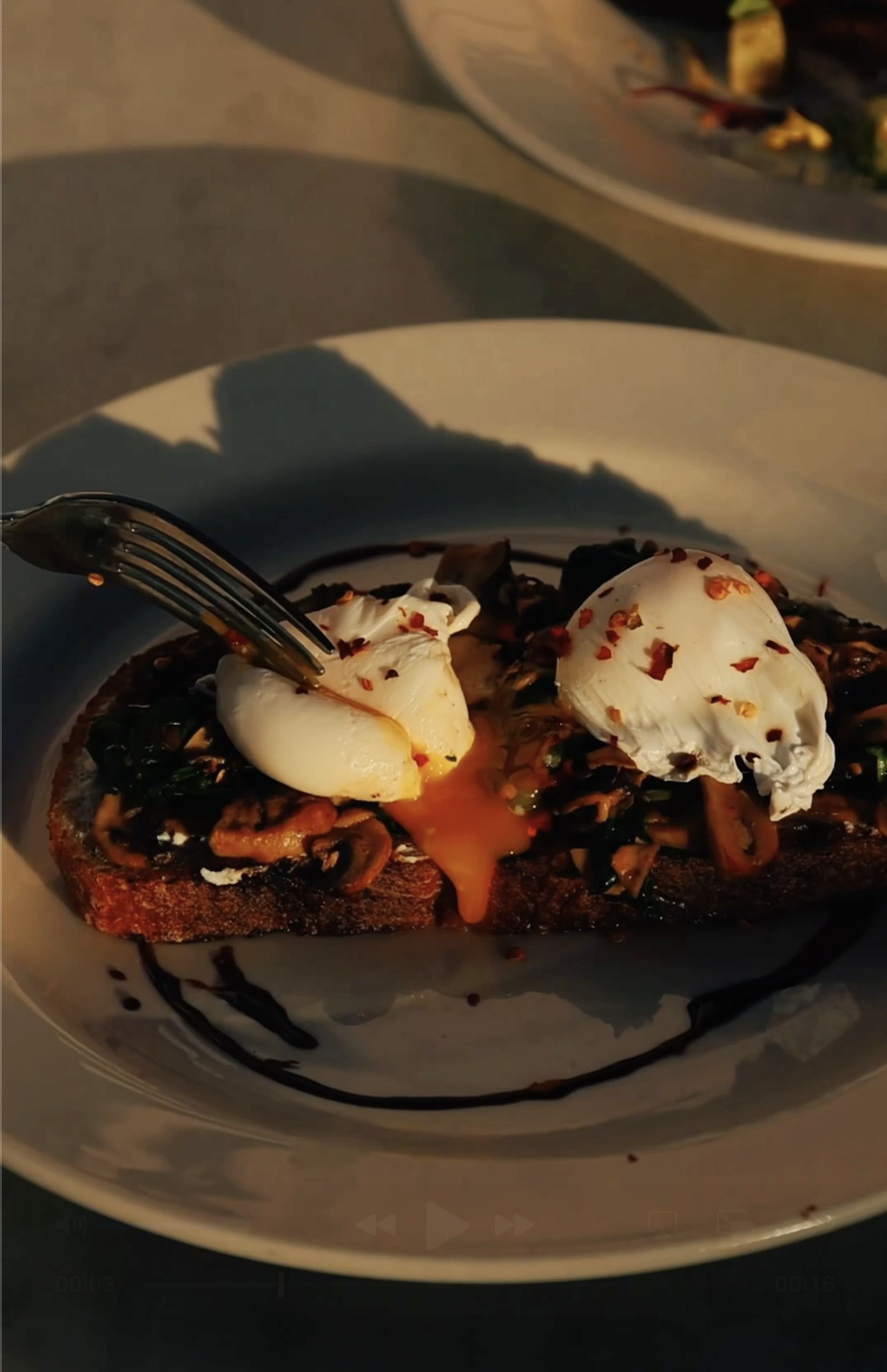 A plate with toast topped with sautéed vegetables, two poached eggs, and drizzled with sauce and red pepper flakes.