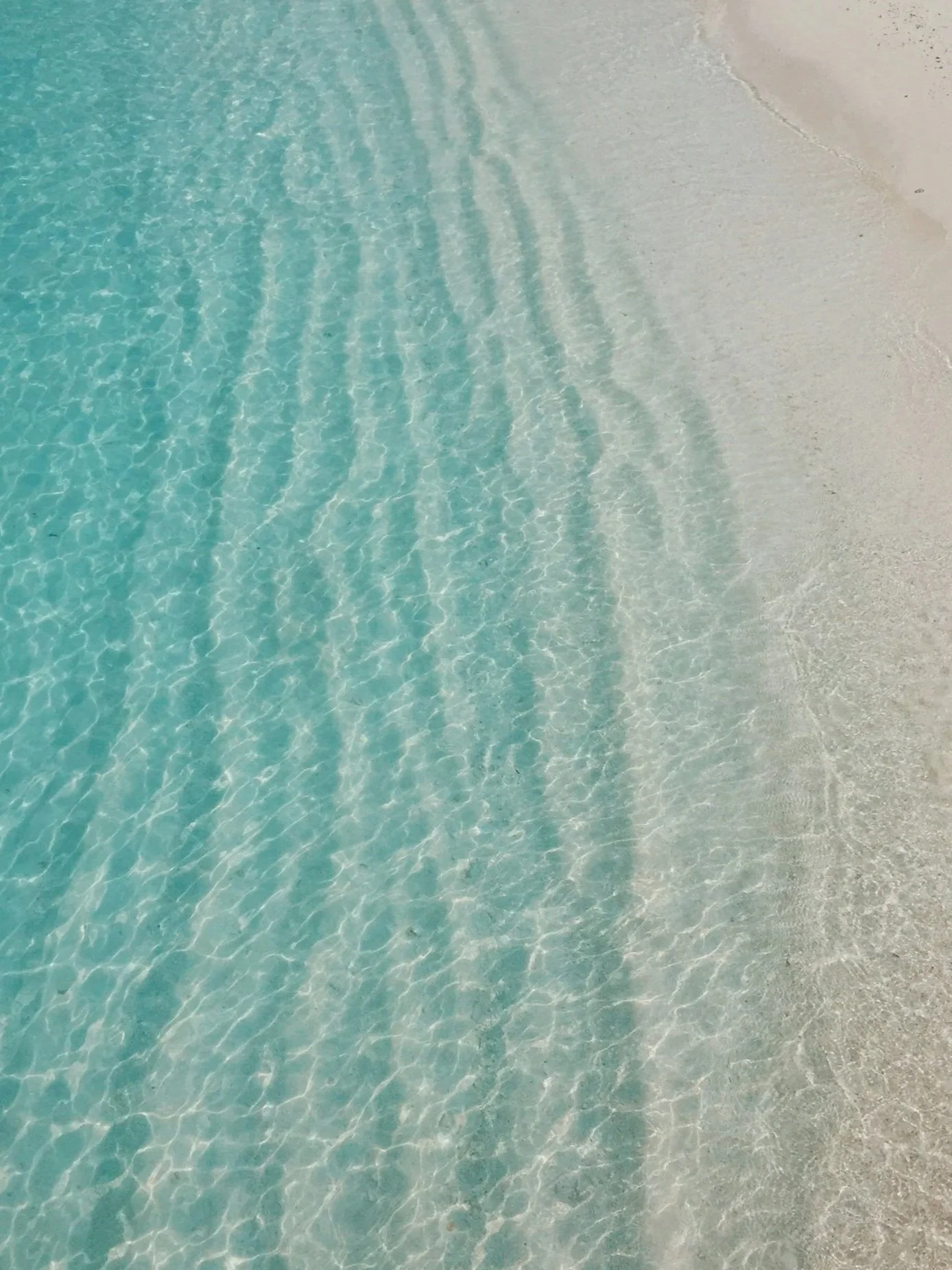 Clear turquoise water gently lapping a white sandy beach.