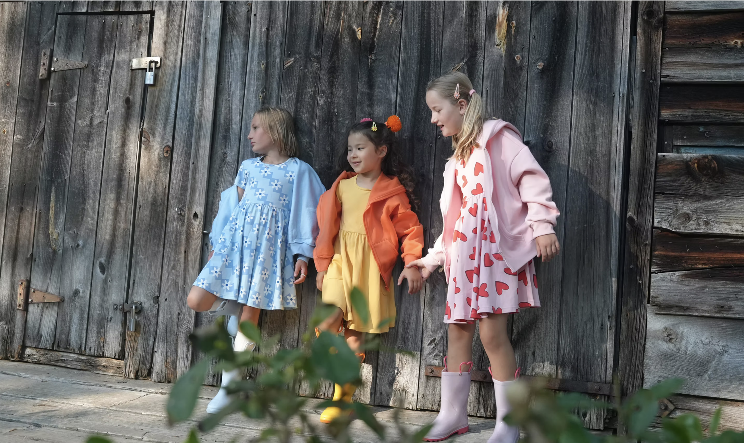 Four young girls holding hands and standing against a rustic wooden barn door.