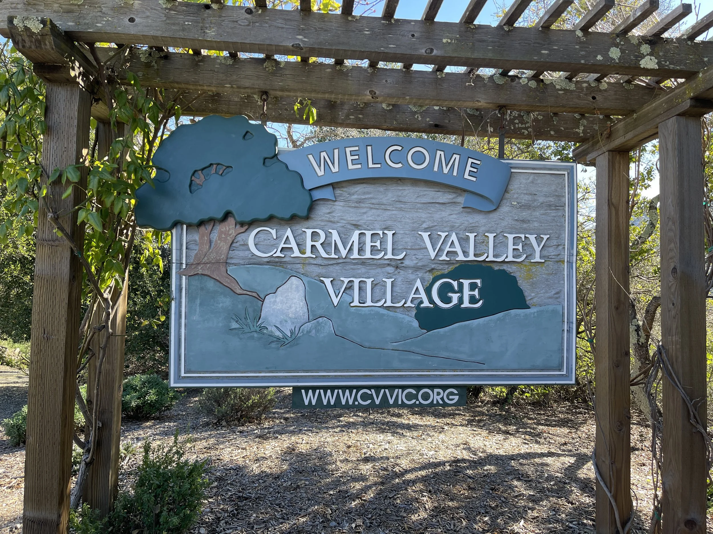 Welcome sign for Carmel Valley Village with a tree illustration and website URL.