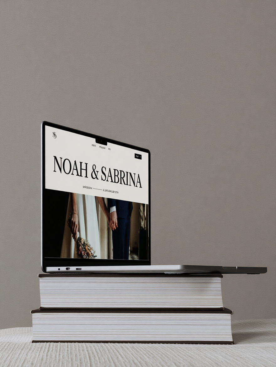 A laptop displaying the website 'Noah & Sabrina' on top of two stacked large books, placed on a white surface against a plain neutral wall.