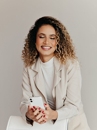 A woman with curly hair smiling and holding a smartphone