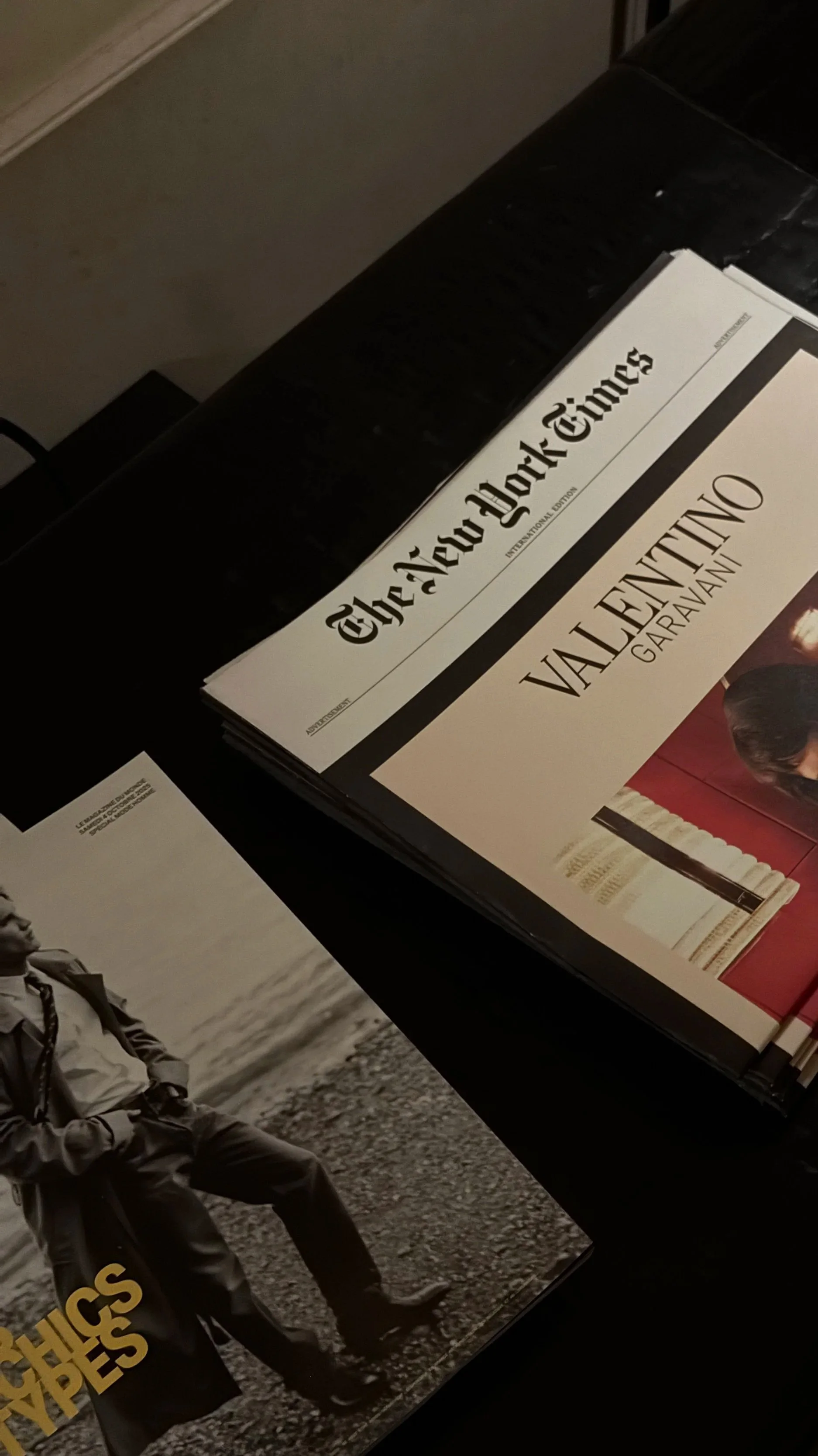 Stack of newspapers, including The New York Times with a headline about Valentino Garavani, and a fashion magazine featuring a person sitting outdoors.