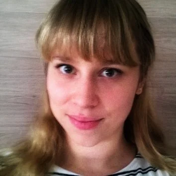 Portret van een jonge vrouw met lichte huid, blond haar en blauwe ogen, lachend voor een houten achtergrond.