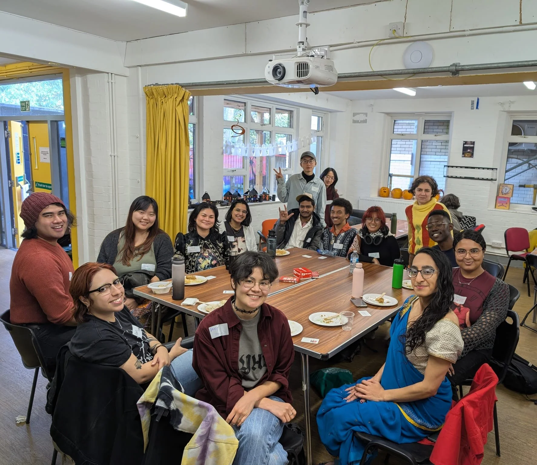 Queer people of colour diverse group of people smiling and enjoying community company. Seated, accessible, decorations, festive Eid, docklands, bristol, docklands community centre
