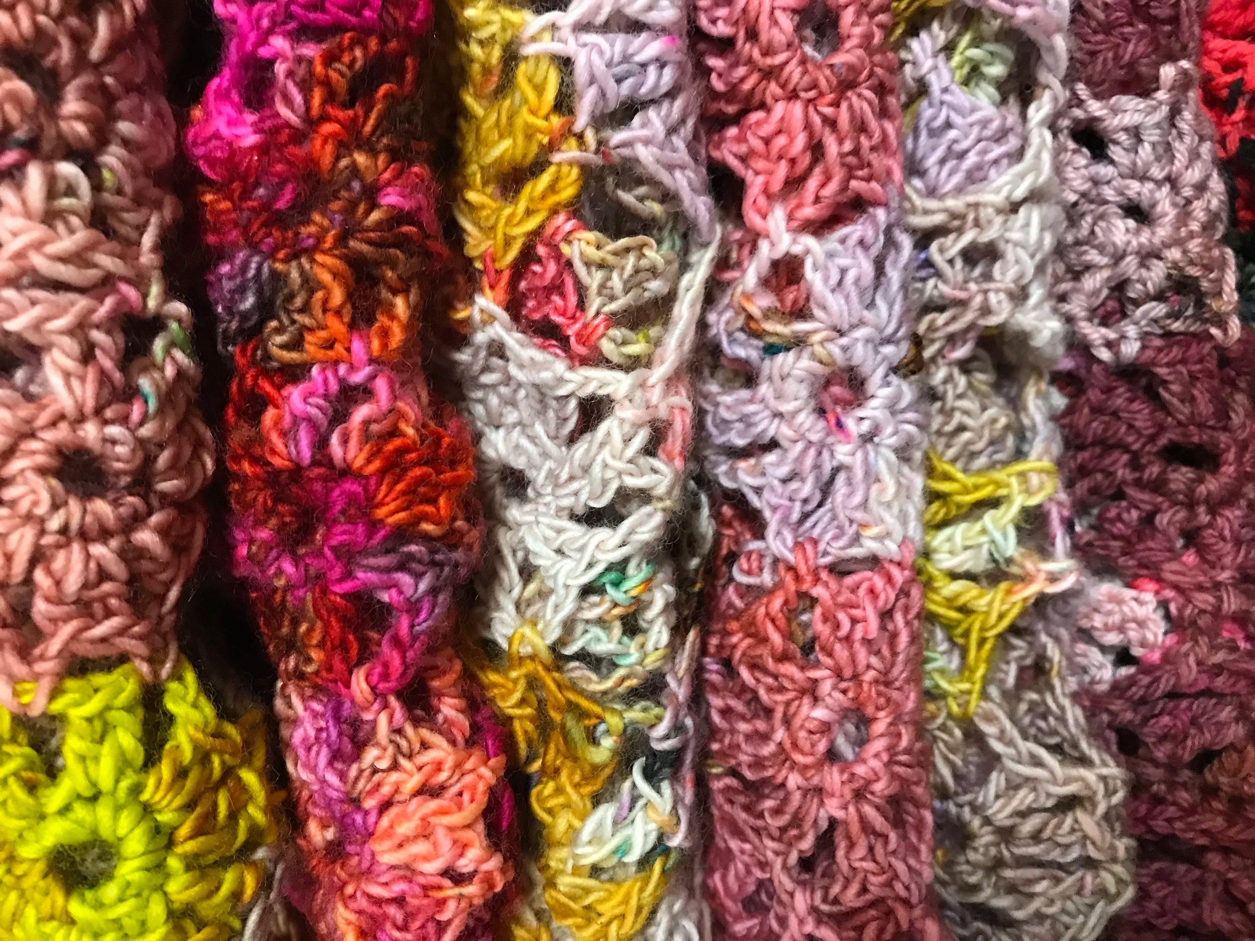 Close-up of colorful, knotted, loosely crocheted or knitted fabric strips in pink, purple, yellow, white, orange, and red.