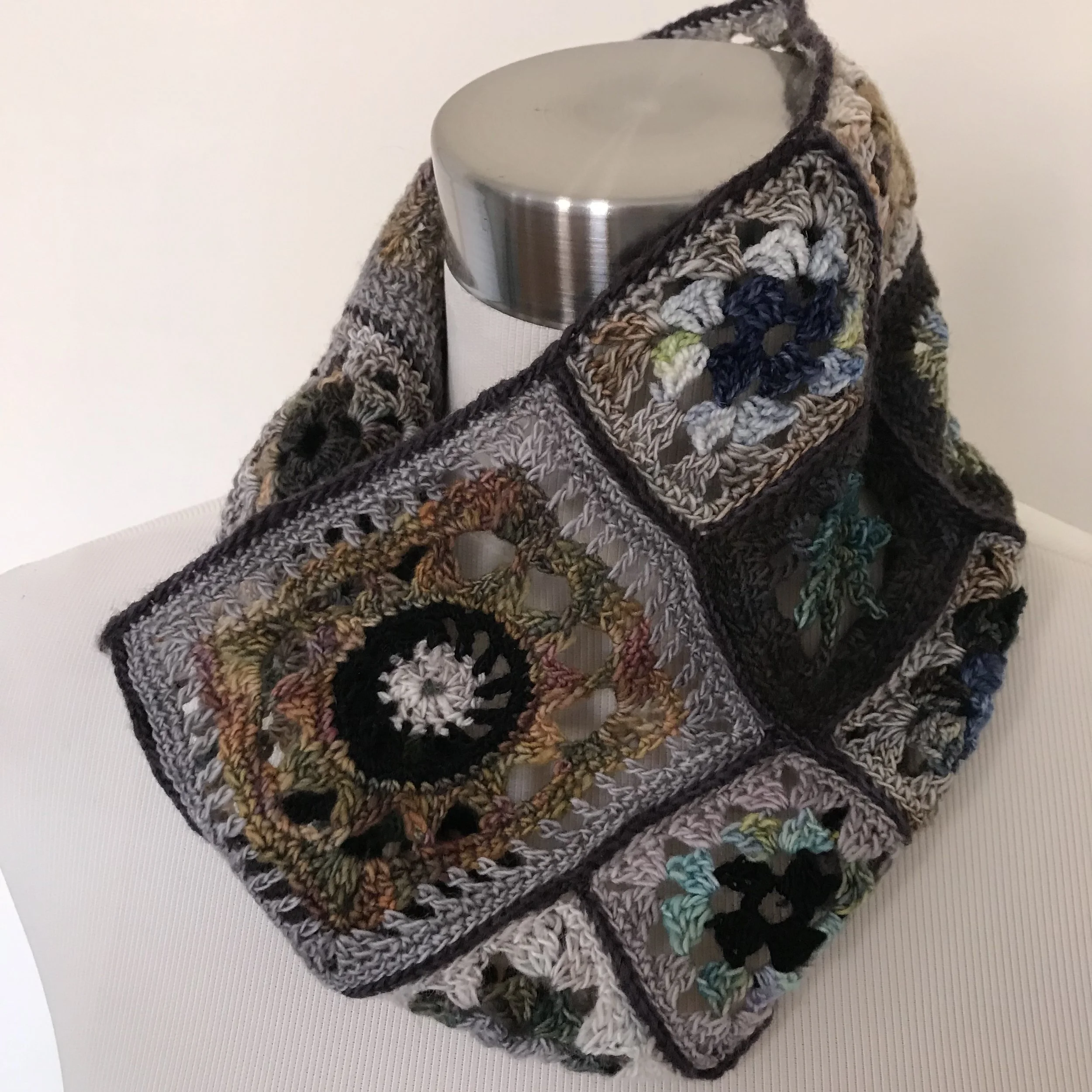 Colorful crochet granny square scarf draped over a metal mannequin stand.