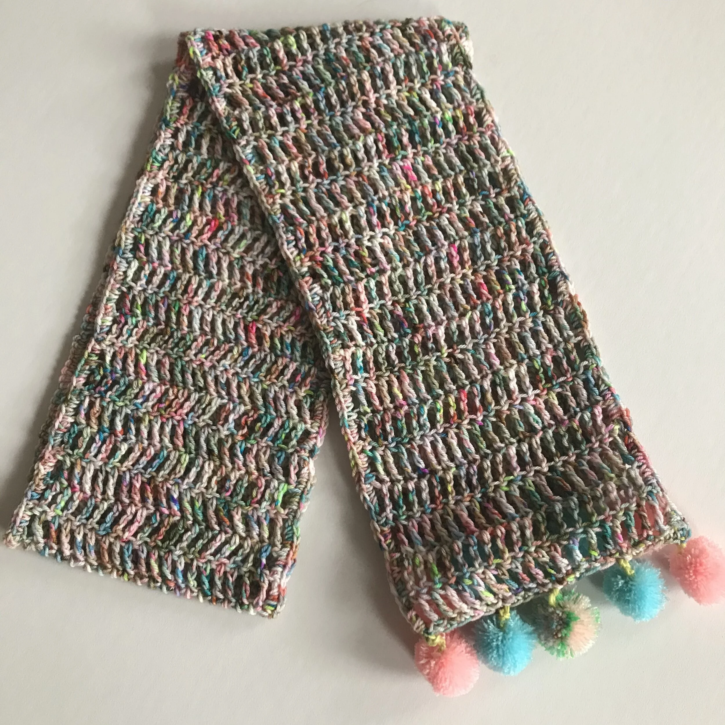 Colorful crocheted scarf with pom-poms on the ends, lying on a white surface.