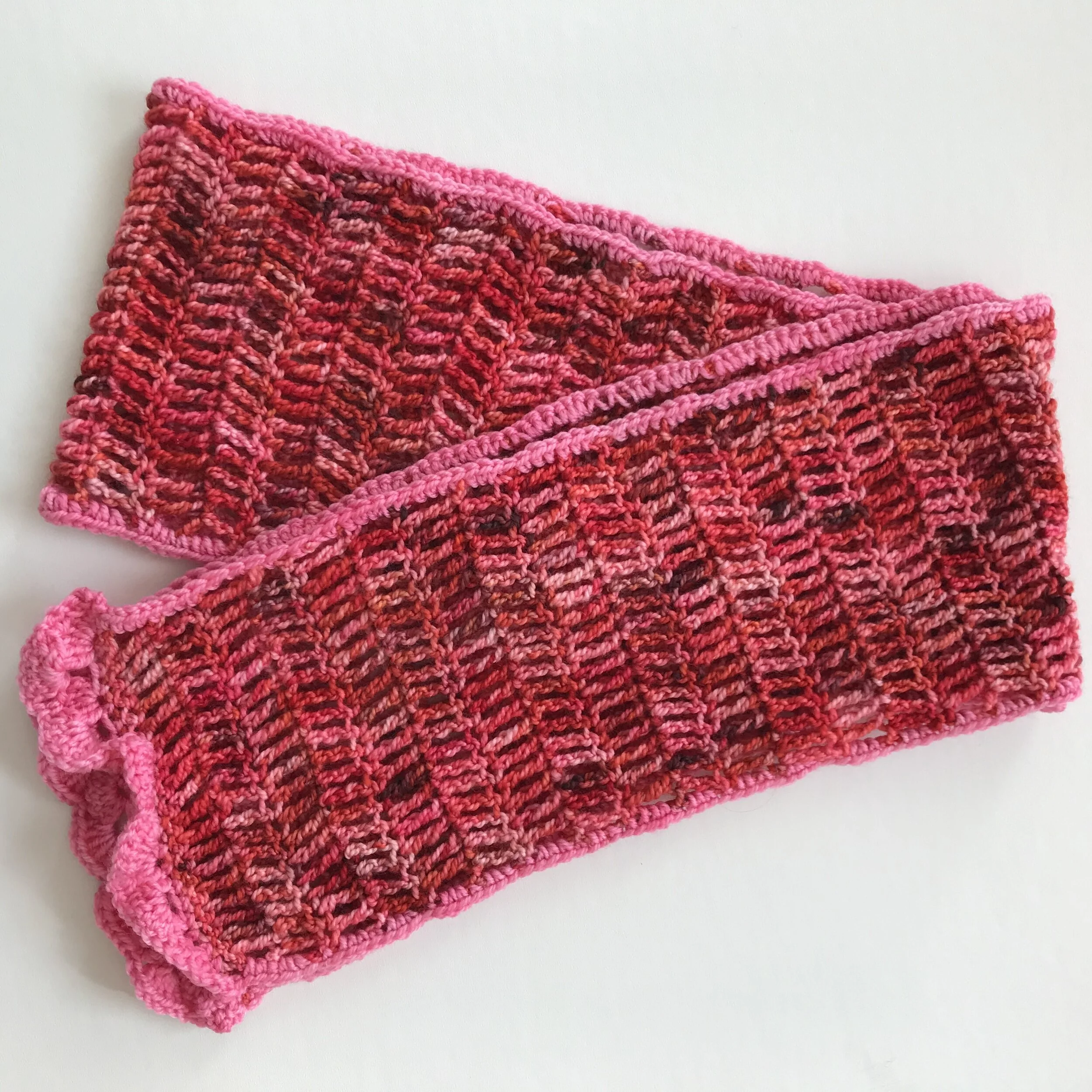 Pair of pink and multicolored knitted wrist warmers with ribbed cuff and openwork pattern.