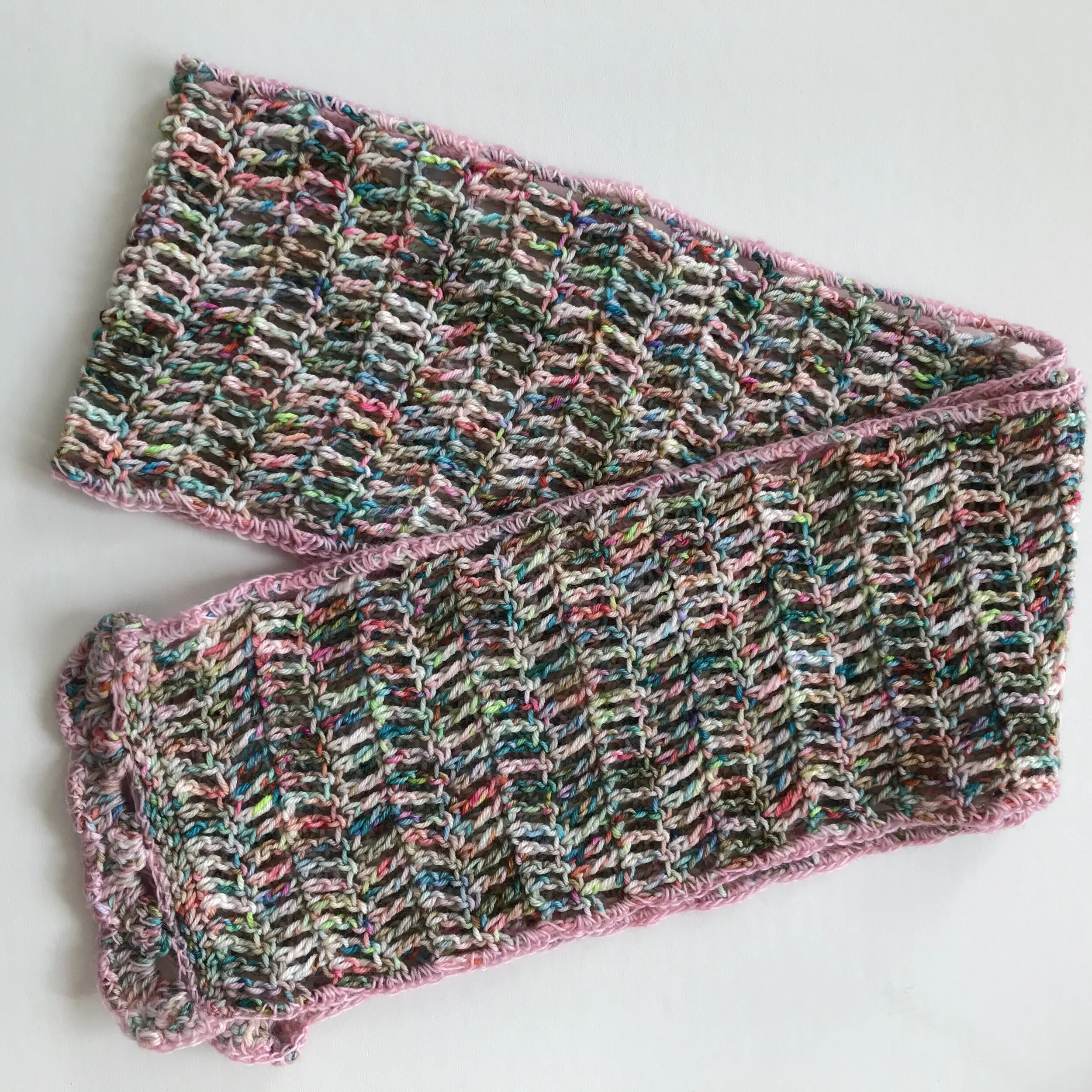 Two colorful hand-knit dishcloths with pink borders, stacked on a white surface.