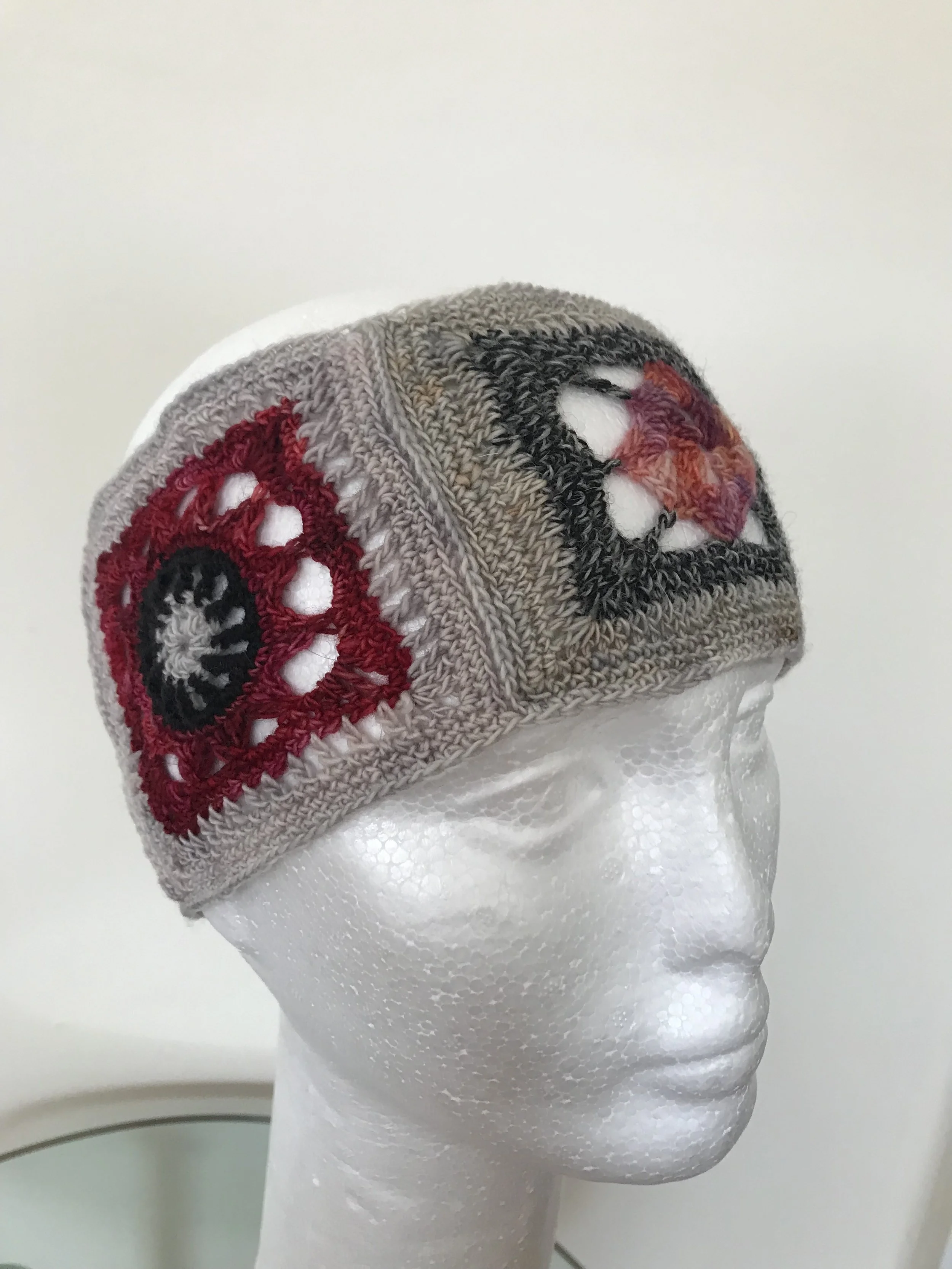 A mannequin head wearing a knitted beanie with embroidered eye and mouth designs.