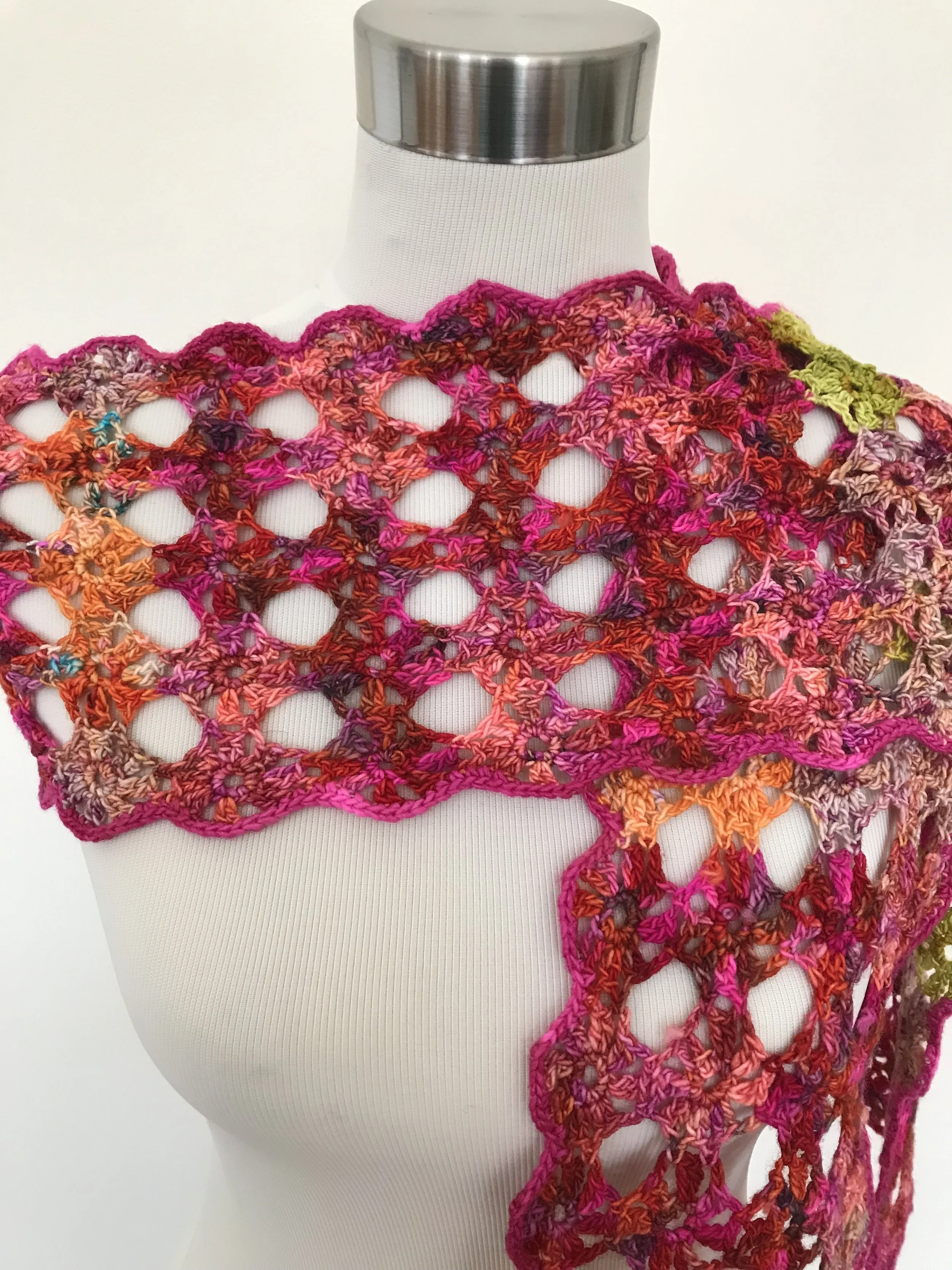 A mannequin torso wearing a colorful, open-knit crochet shawl in shades of pink, orange, purple, and green.