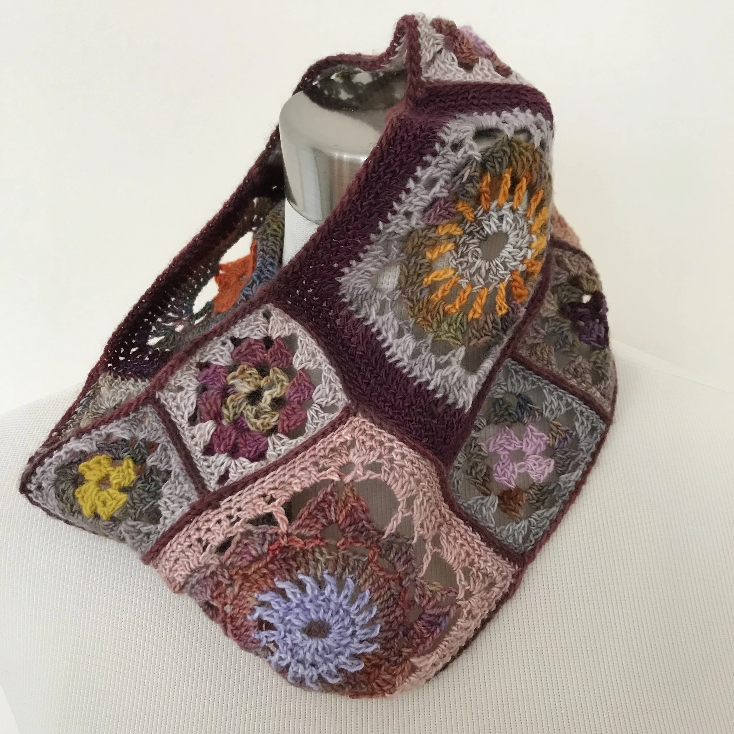 A crochet blanket with colorful granny square patterns draped over a mannequin bust.