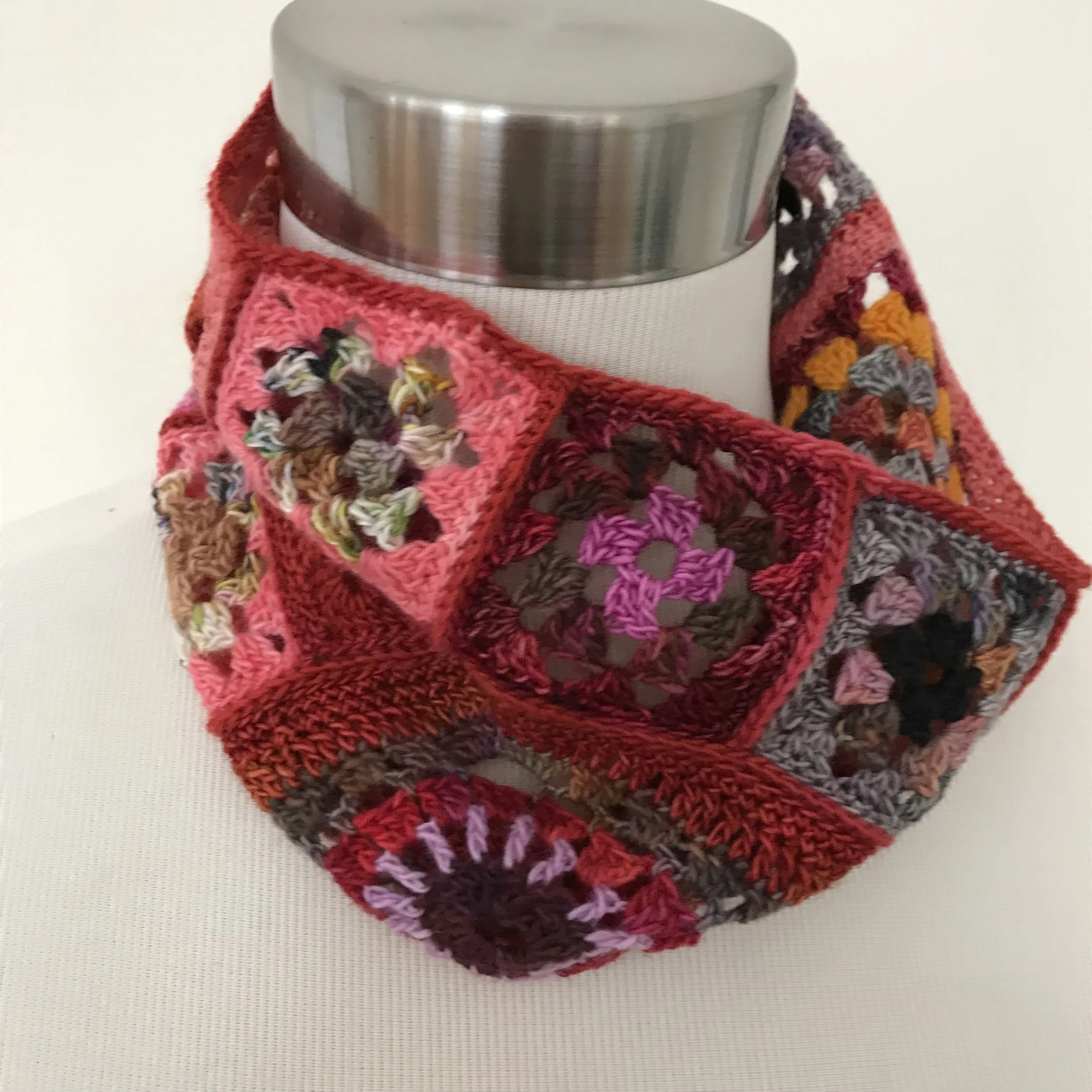 Metal thermos wrapped with a colorful crocheted cozy featuring various granny square patterns.