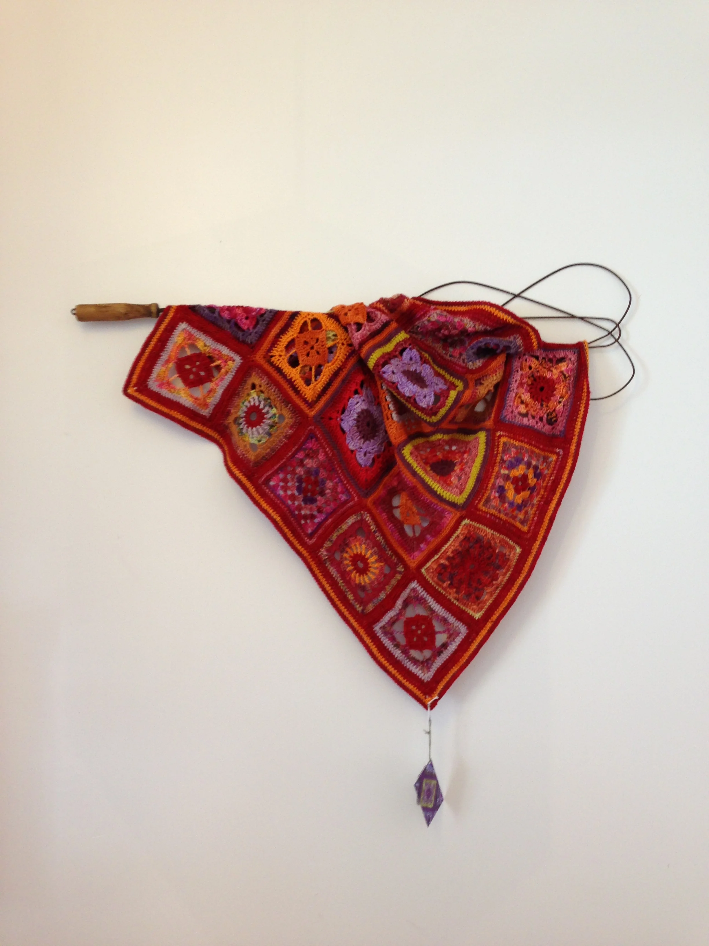 Colorful crocheted banner with patterned squares and a purple and yellow diamond-shaped decoration hanging at the bottom.